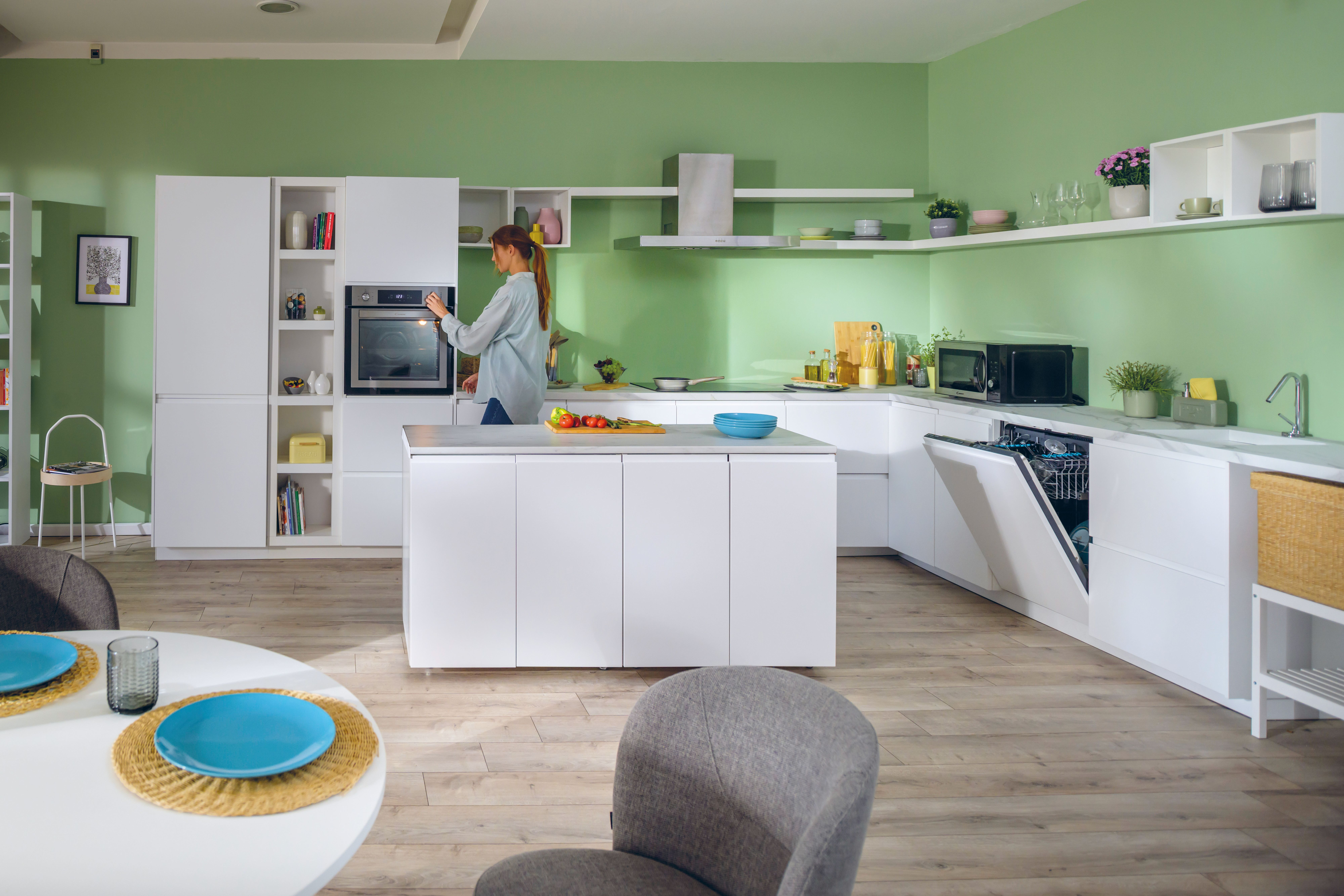 Una donna in una cucina moderna è in piedi vicino a un forno. C'è un tavolo con piatti e cibo sul bancone.