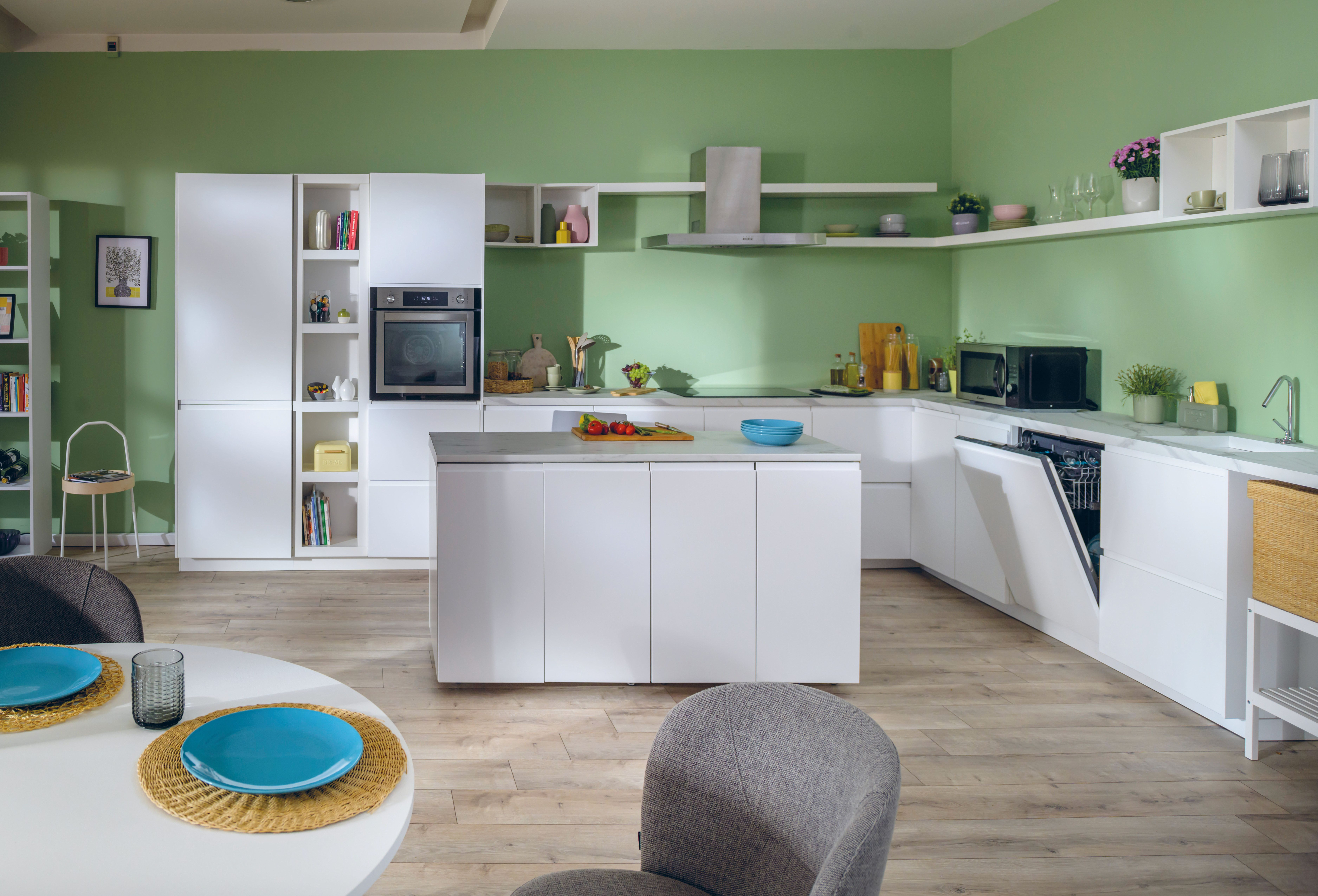Una cucina moderna con mobili bianchi, pareti verdi, pavimento in legno e tavolo con piatti blu.