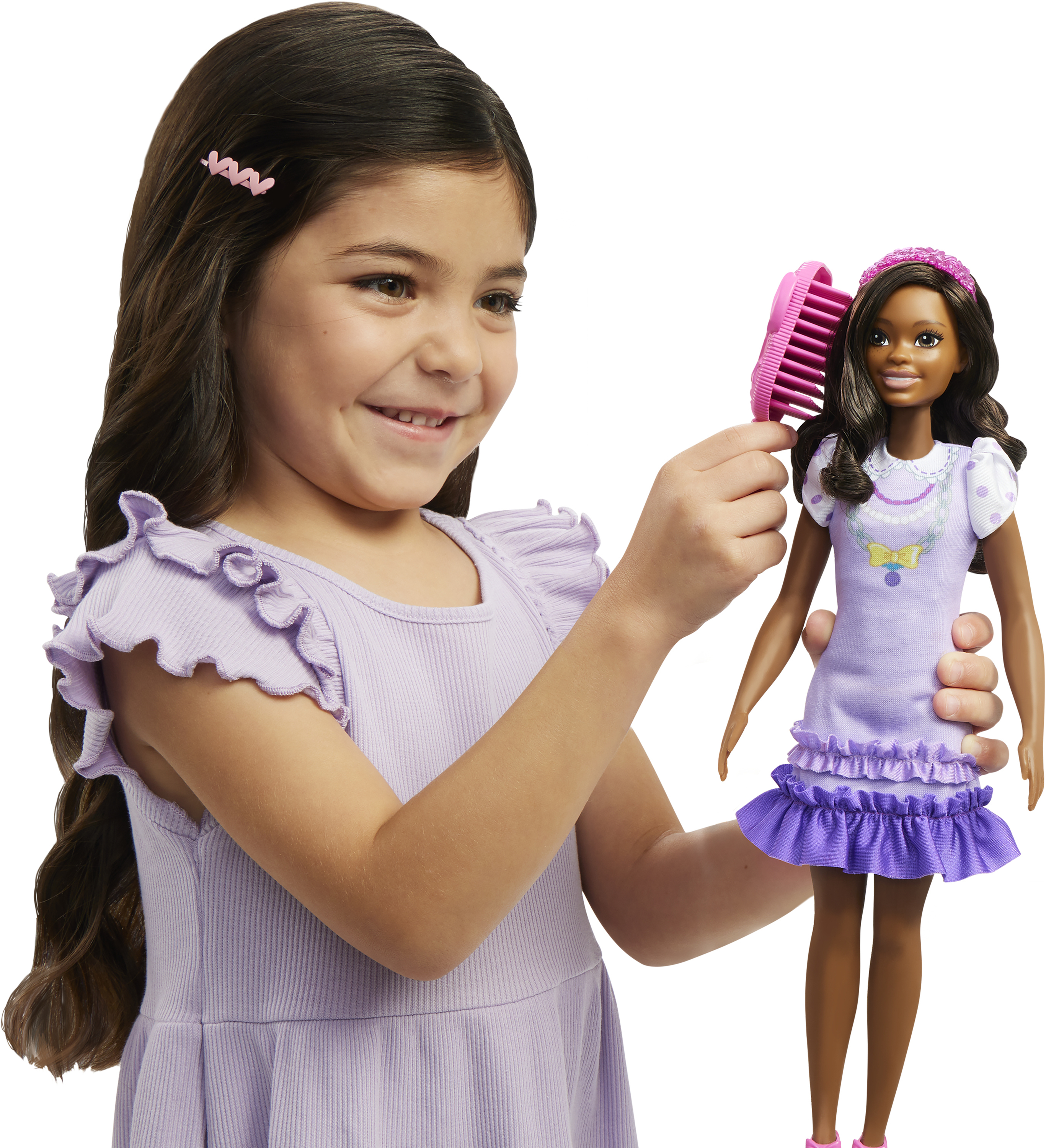 Una niña cepilla el pelo de una muñeca. Ambas sonríen. La muñeca lleva un vestido morado.