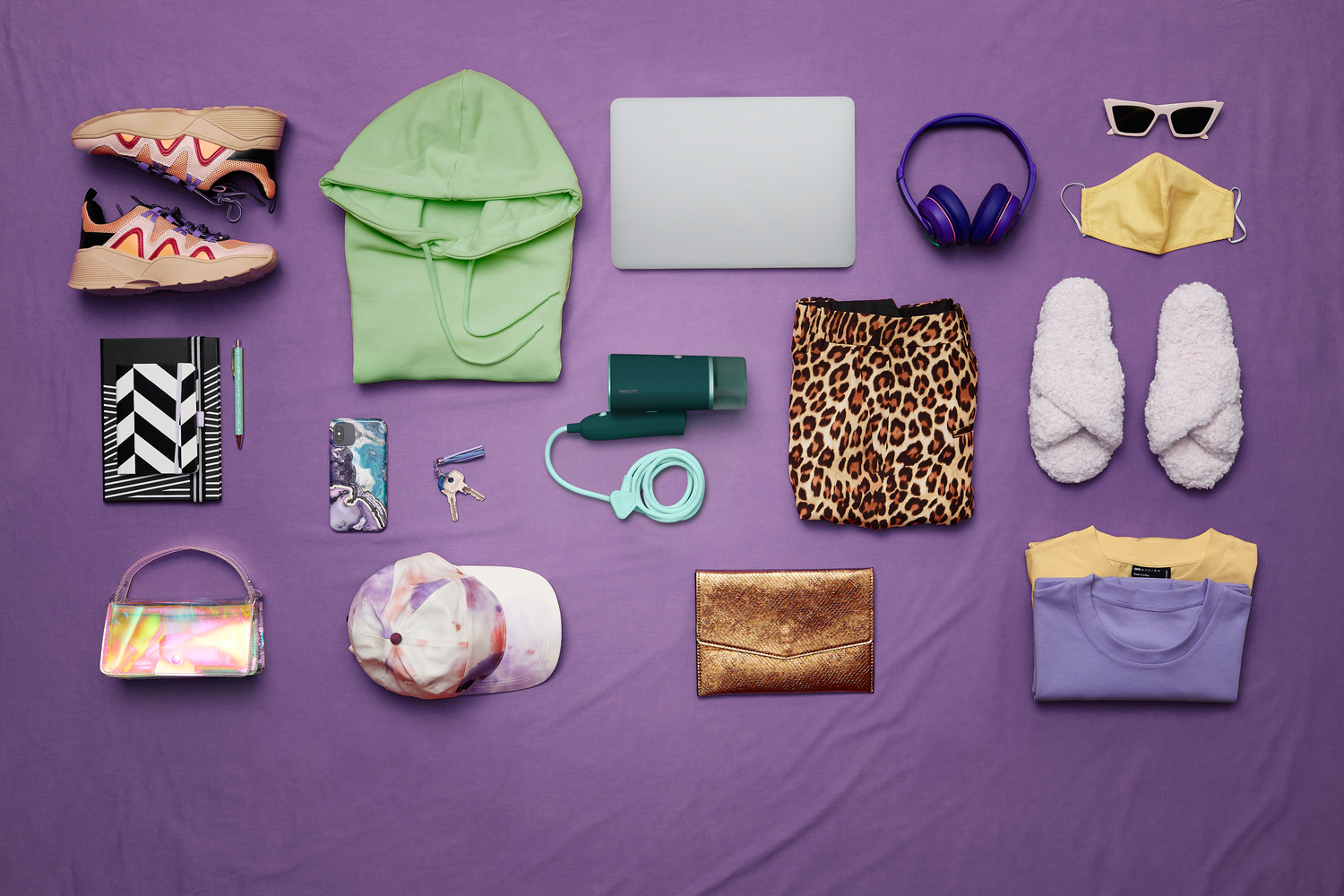 Sammlung von Gegenständen auf lila Hintergrund: Schuhe, Kapuzenpullover, Laptop, Kopfhörer, Maske, Rock, Hausschuhe, Tasche, Mütze, Schlüssel und Kleidung.