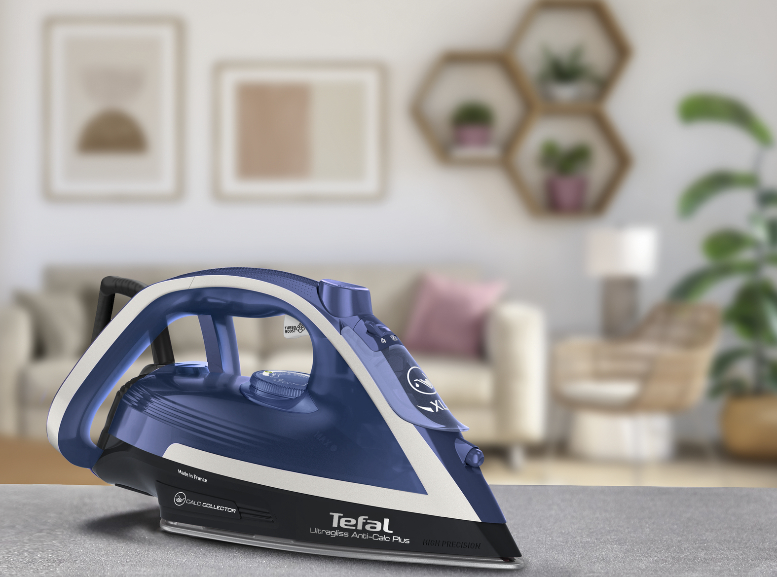Ein blaues und weißes Tefal-Bügeleisen auf einer grauen Oberfläche, mit verschwommenem Wohnzimmerhintergrund.