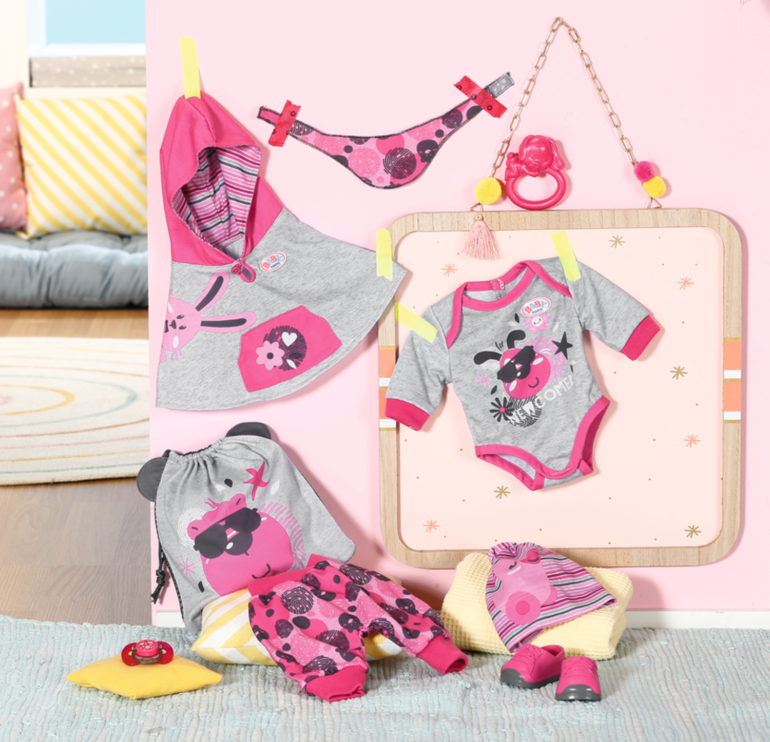 Babykleidung und Accessoires auf rosa Hintergrund. Enthält einen Hoodie, einen Strampler, eine Hose, eine Tasche, Schuhe und einen Schnuller.