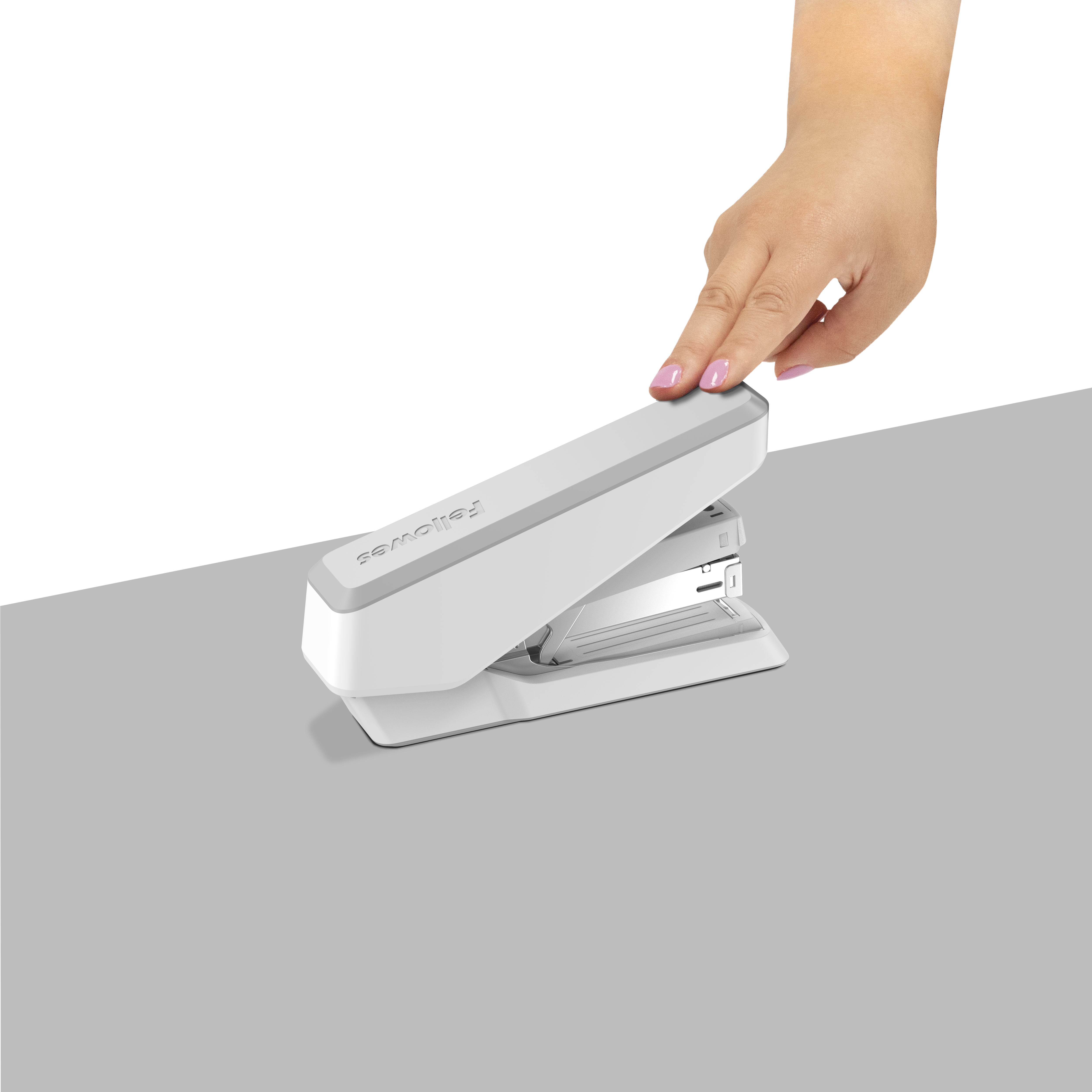 Eine Hand drückt auf einen weißen Tacker, der auf einer grauen Oberfläche vor weißem Hintergrund liegt.