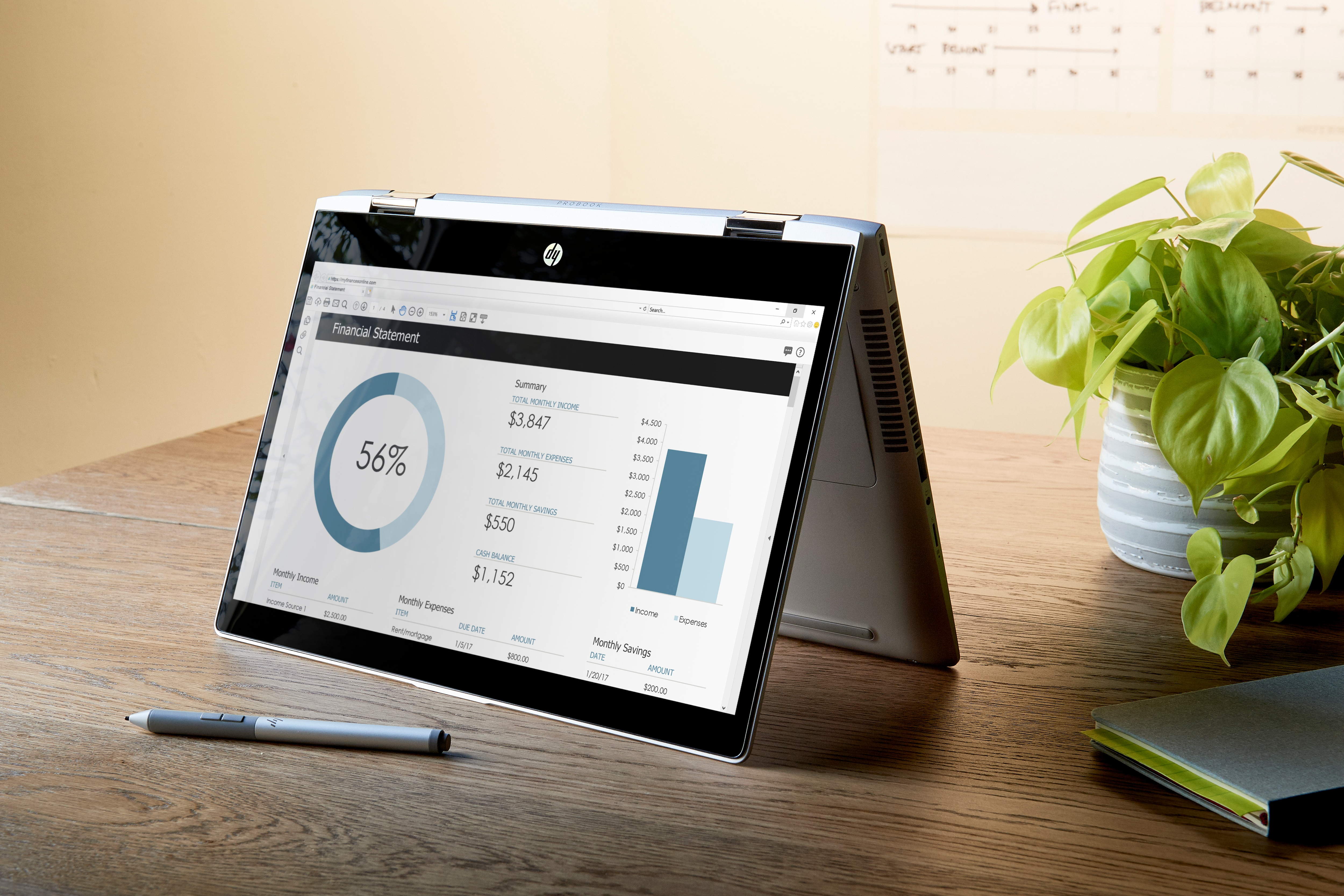 Laptop wyświetla zestawienie finansowe. Na drewnianym biurku roślina i notatnik.