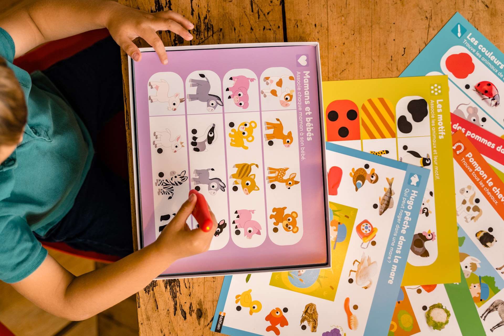 Dziecko gra w grę polegającą na dopasowywaniu obrazków zwierząt. Gra znajduje się na drewnianym stole, z kolorowymi kartami dookoła.