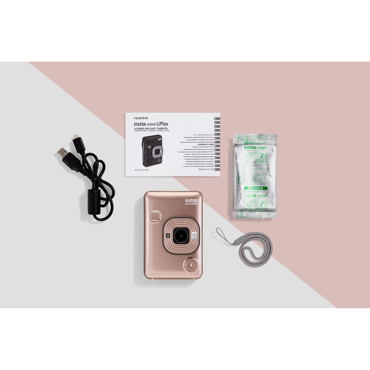Una cámara Instax mini LiPlay de oro rosa, un cable USB, un paquete de película, un manual y una correa de muñeca están colocados sobre una superficie blanca y rosa.