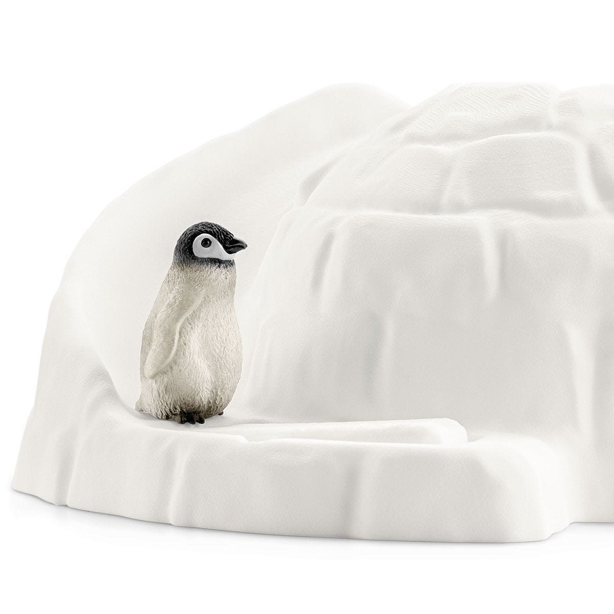 Un pingouin se tient sur une plateforme enneigée devant un igloo blanc. Le pingouin a des marques noires et blanches.