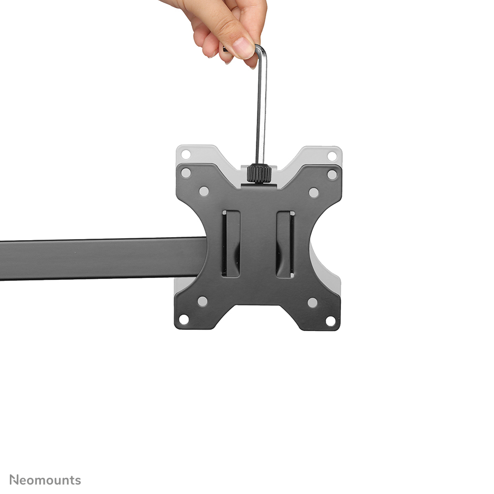 Een hand houdt een zilveren gereedschap boven een zwarte metalen beugel. De beugel heeft gaten en twee verticale sleuven, met een lange arm.