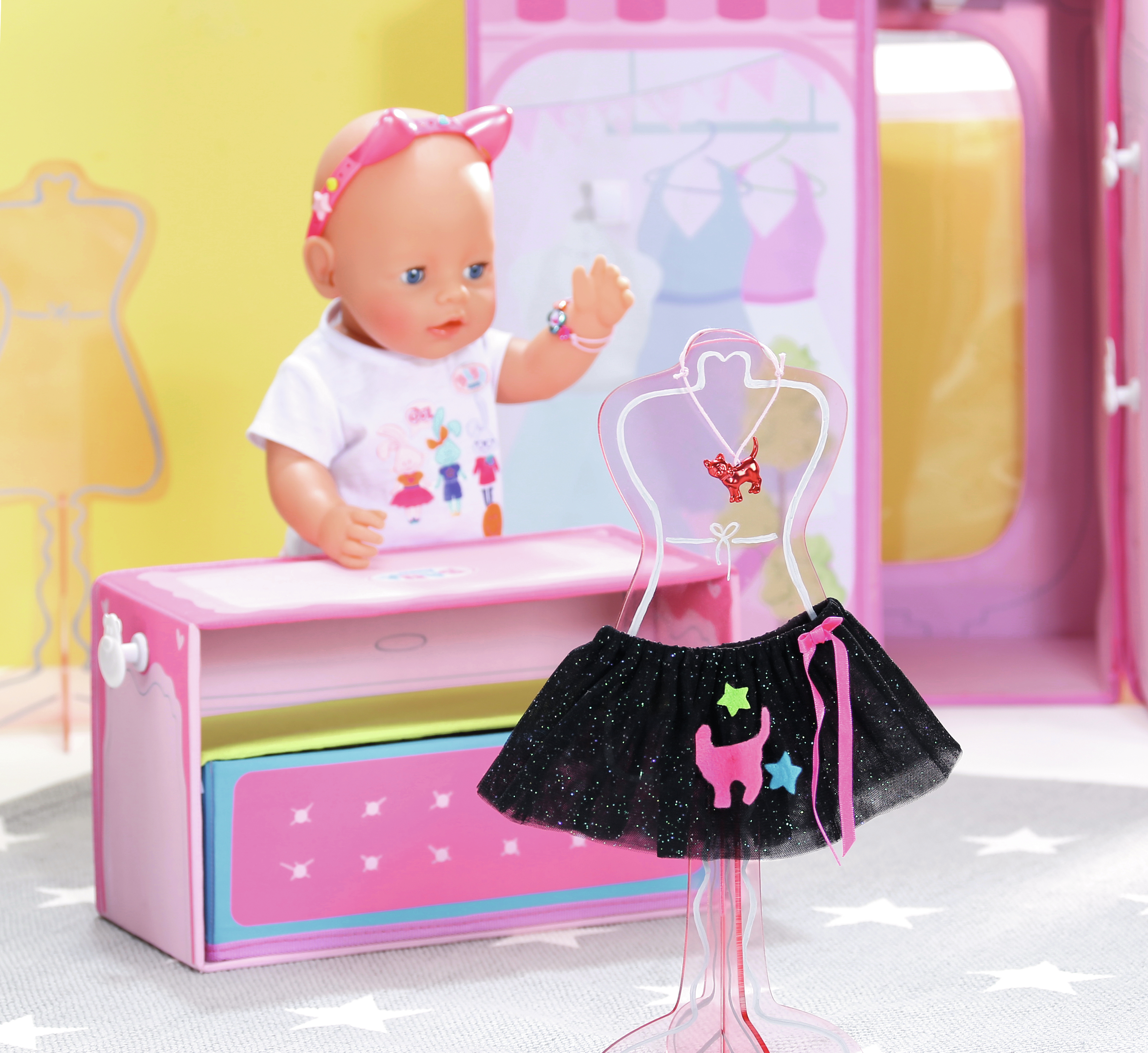 Lalka stoi obok różowej szafy. Czarna spódnica z detalami kota i gwiazdy stoi przed nią.