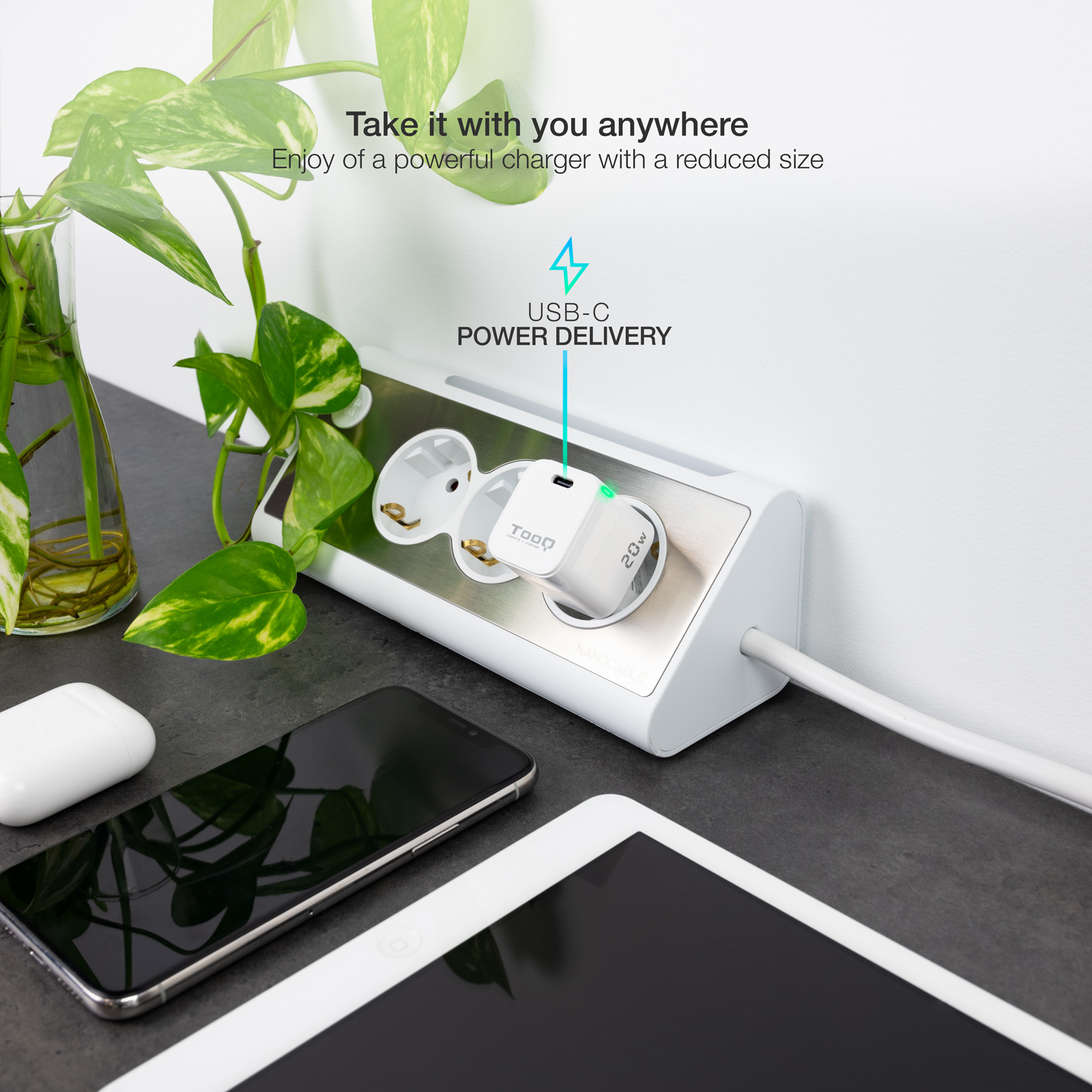 Una regleta blanca con un cargador enchufado, un teléfono, una tableta y una planta.