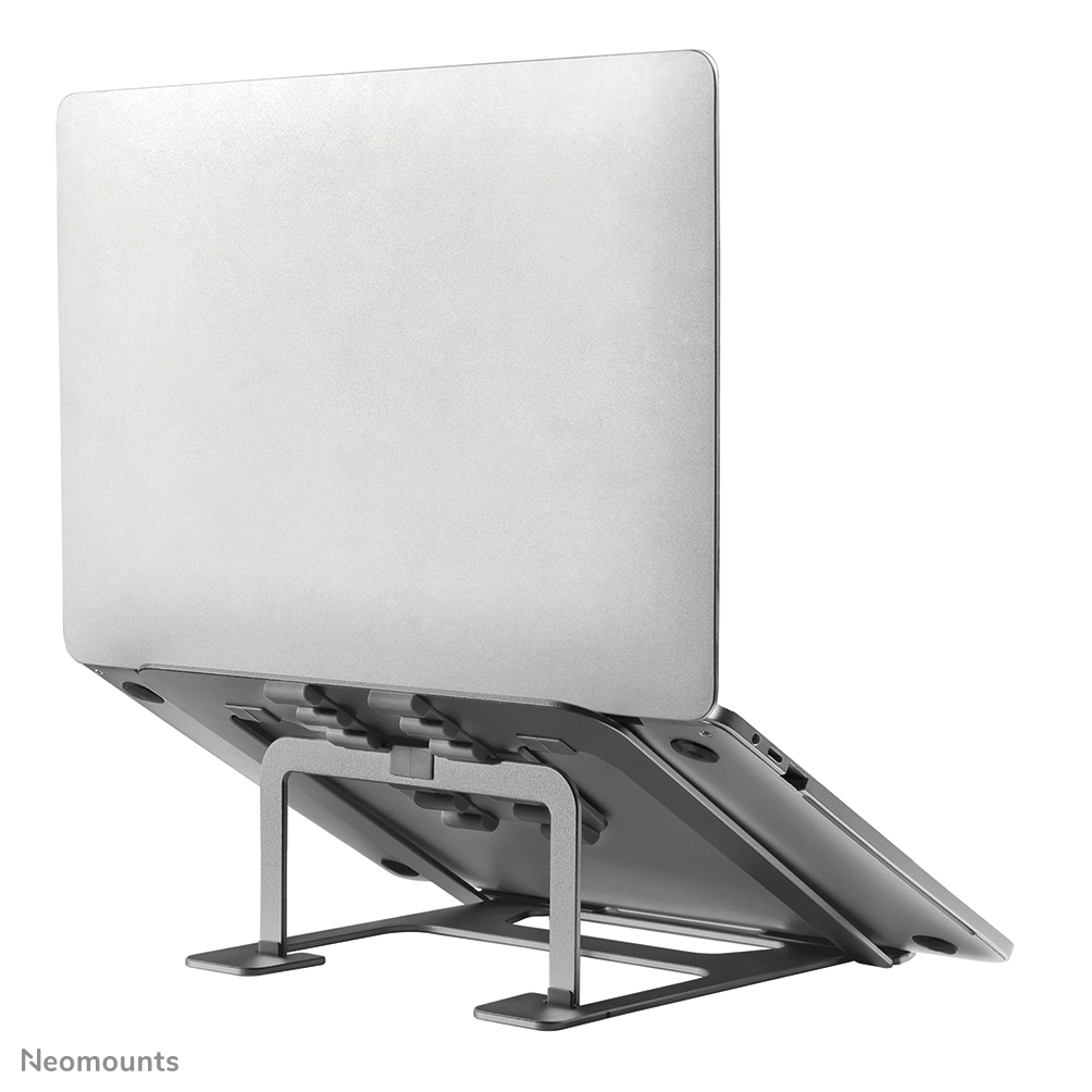A silver laptop is placed on a metal stand. The laptop is angled, showing the back and partially the bottom. The stand is also silver.