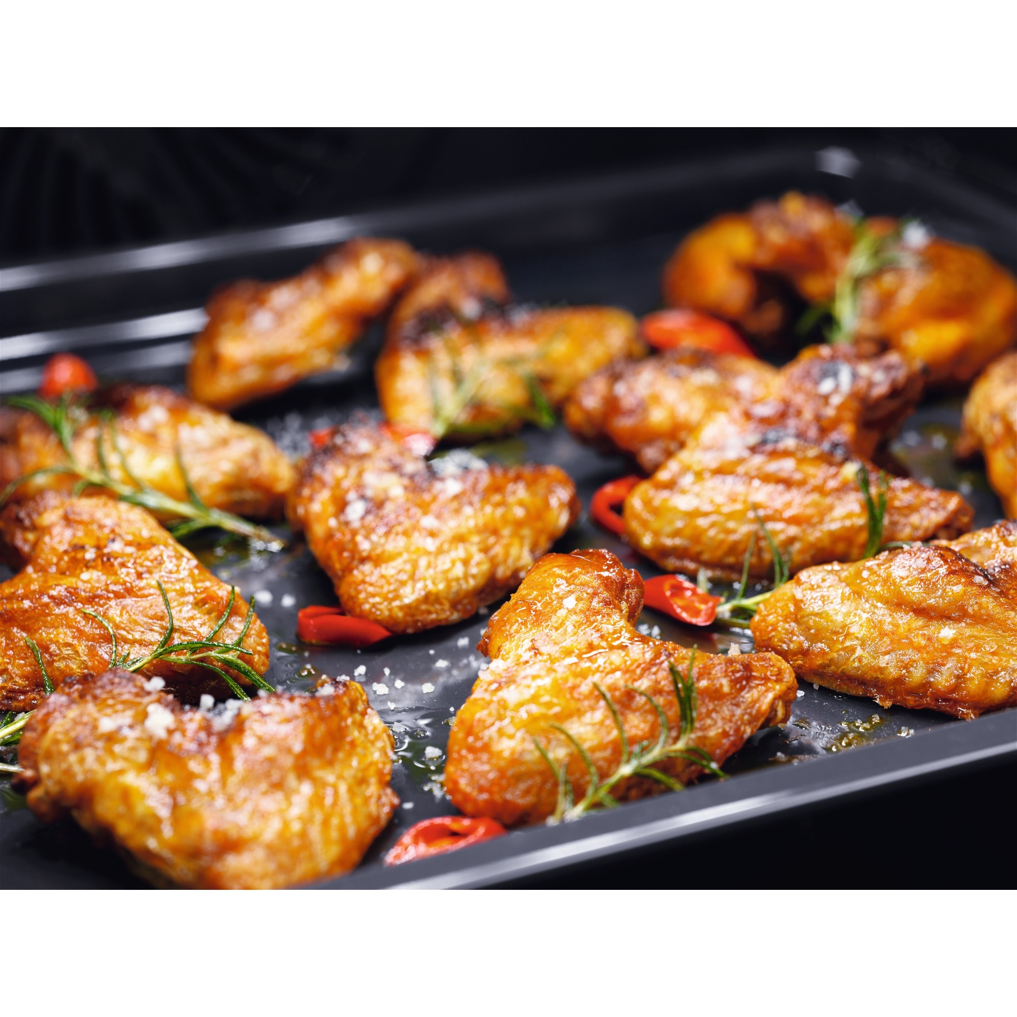 Ali di pollo arrosto su un vassoio, condite con sale, rosmarino e peperoncini rossi. Primo piano, appetitoso.