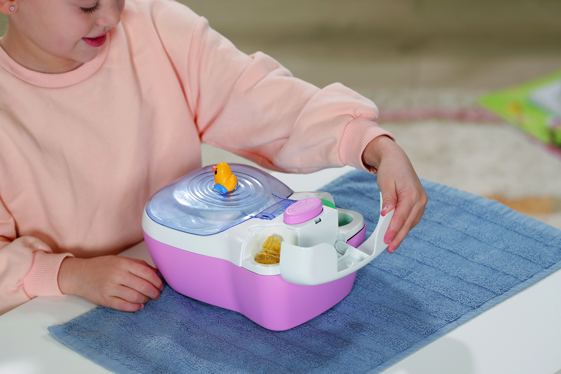 Dziecko bawi się zabawką spa. Żółta kaczka unosi się w wodzie. Zabawka jest różowa i biała.