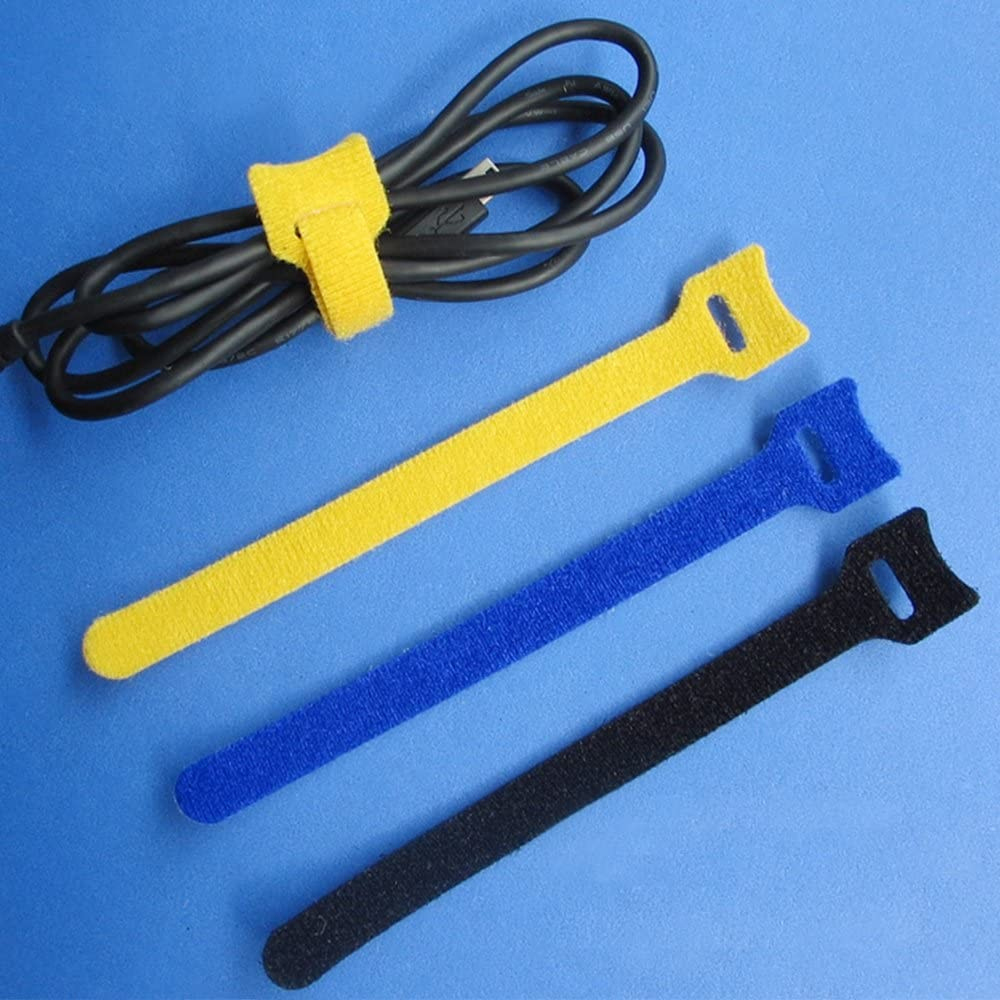 Schwarzes Kabel mit gelbem Klettverschluss gesichert. Drei Klettbänder: gelb, blau und schwarz, liegen auf blauem Untergrund.
