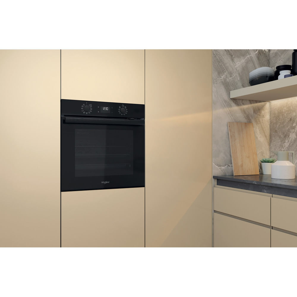 Nowoczesna kuchnia z wbudowanym czarnym piekarnikiem. Widoczne beżowe szafki i backsplash z wzorem marmuru. Deska do krojenia i dekoracje na półce.