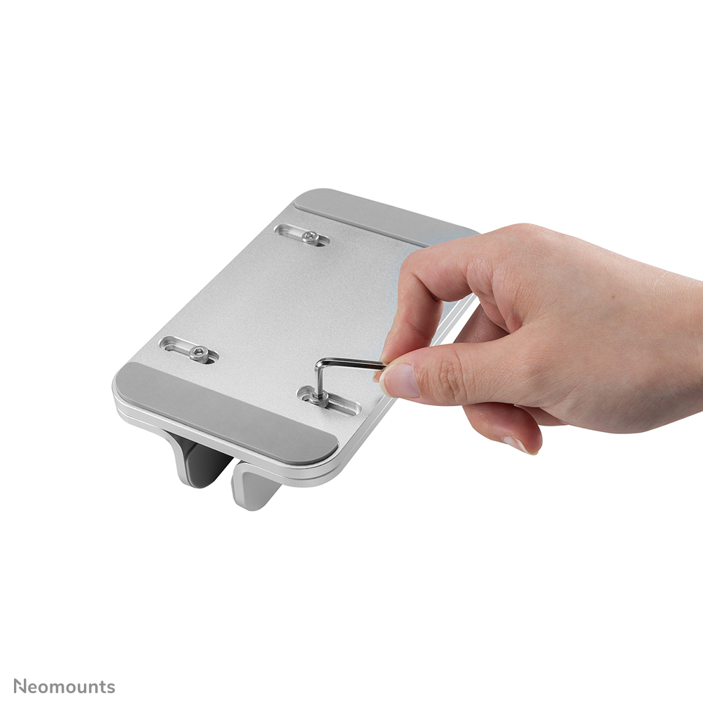A hand using a wrench to tighten a screw on a silver laptop stand. White background.