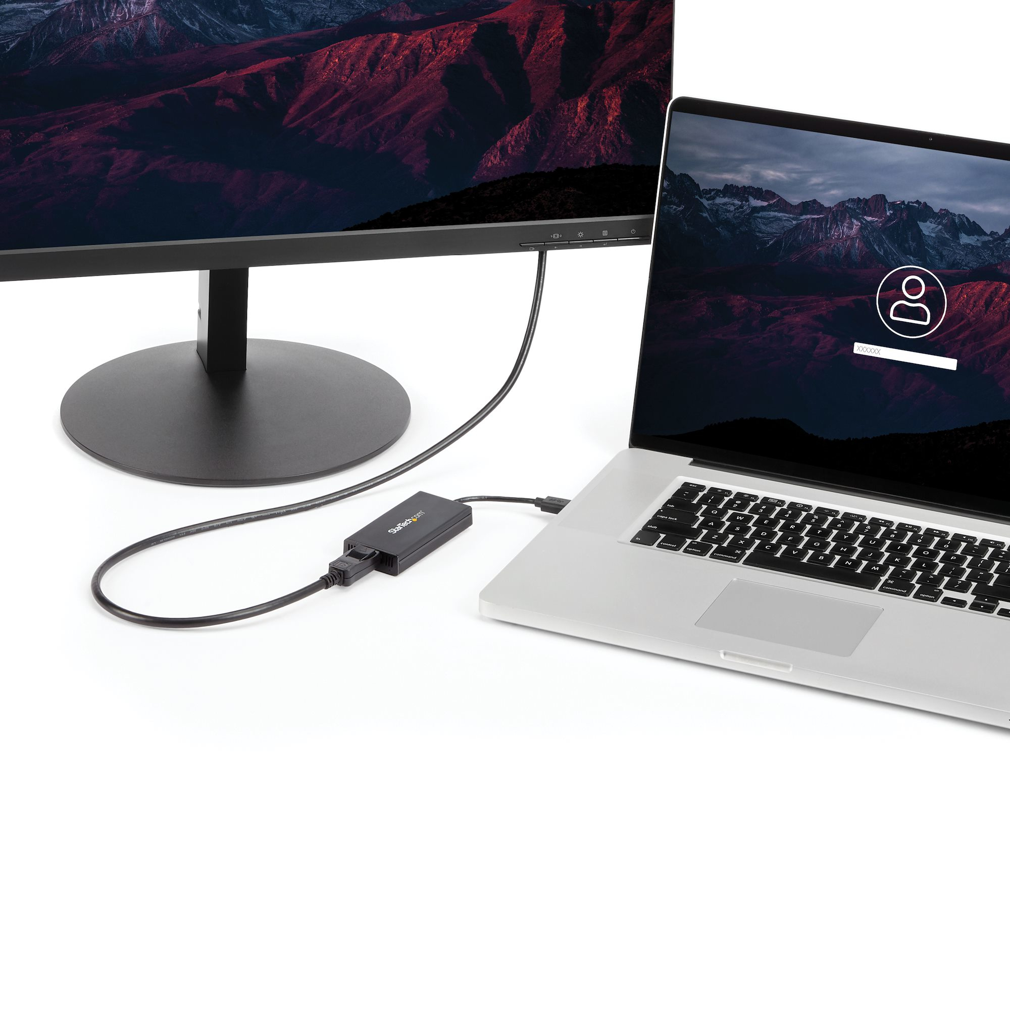 Una laptop y un monitor conectados por un adaptador negro. Ambas pantallas muestran paisajes montañosos.