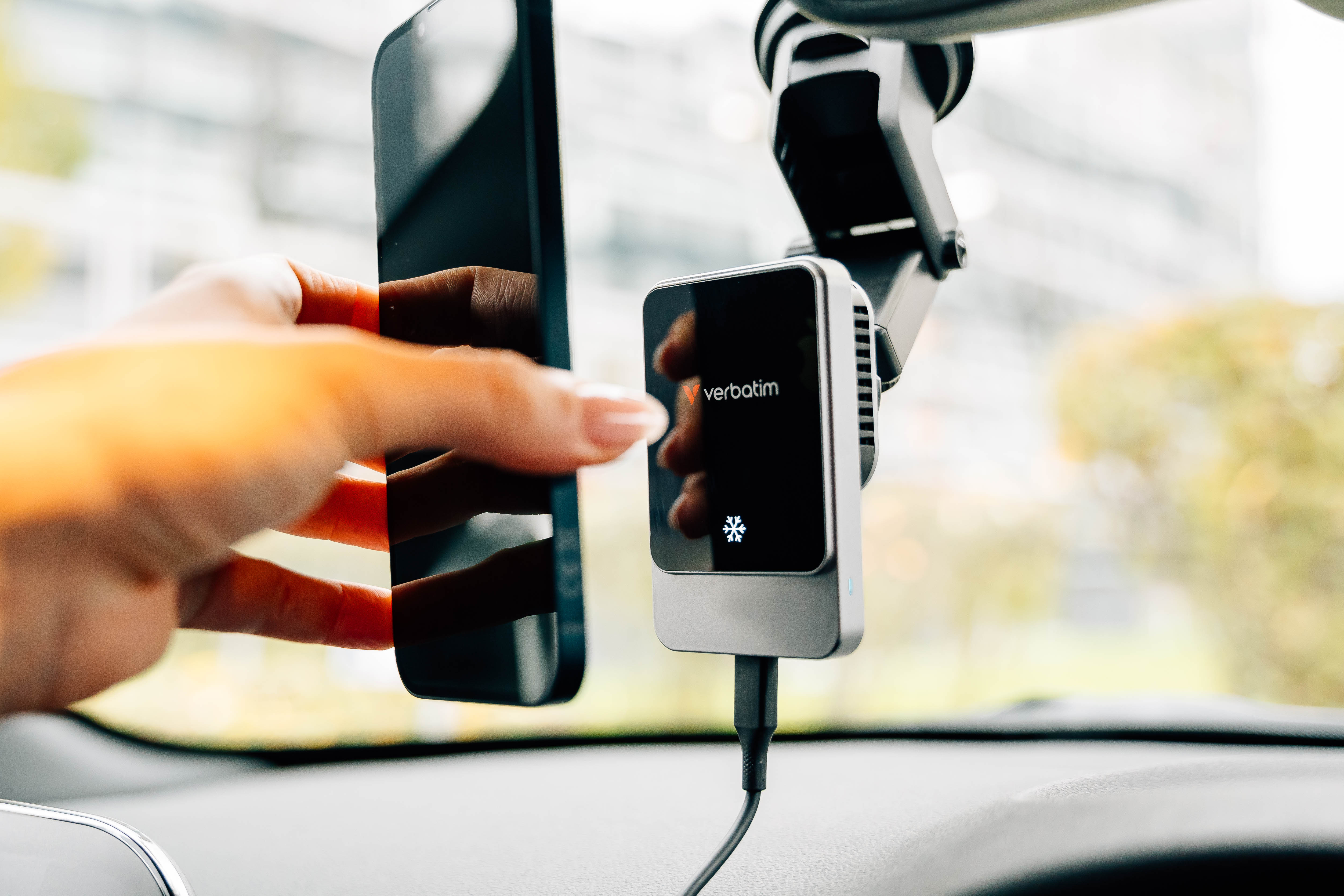 Hand, die ein Telefon neben einem Verbatim-Gerät in einem Auto hält. Das Gerät zeigt ein Schneeflocken-Symbol.