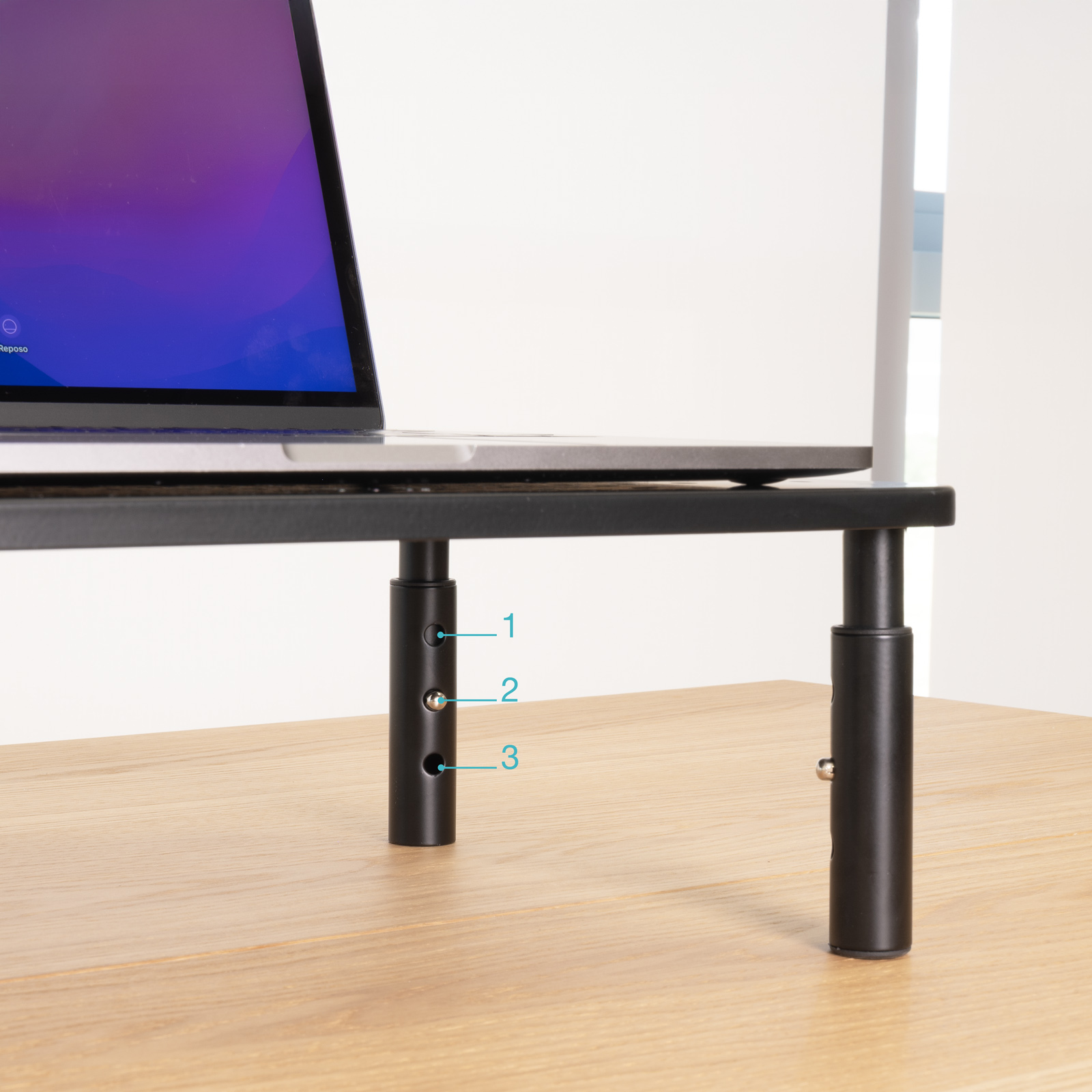 Un laptop è su un supporto nero su un tavolo di legno. Il supporto ha impostazioni di altezza regolabili.