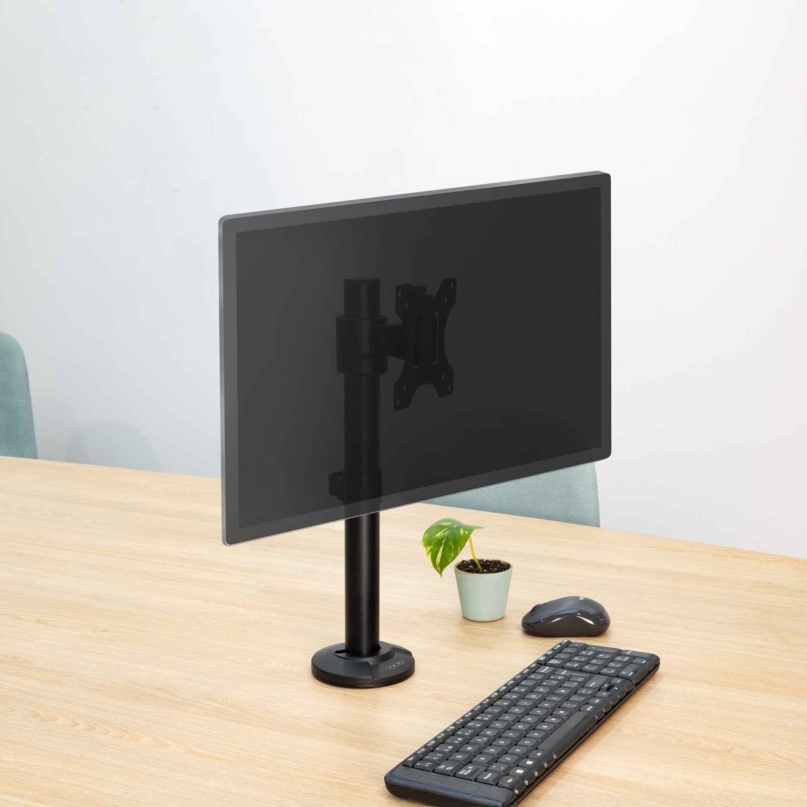 Un monitor per computer su un supporto nero su una scrivania di legno. Tastiera, mouse e pianta sono anche sulla scrivania.