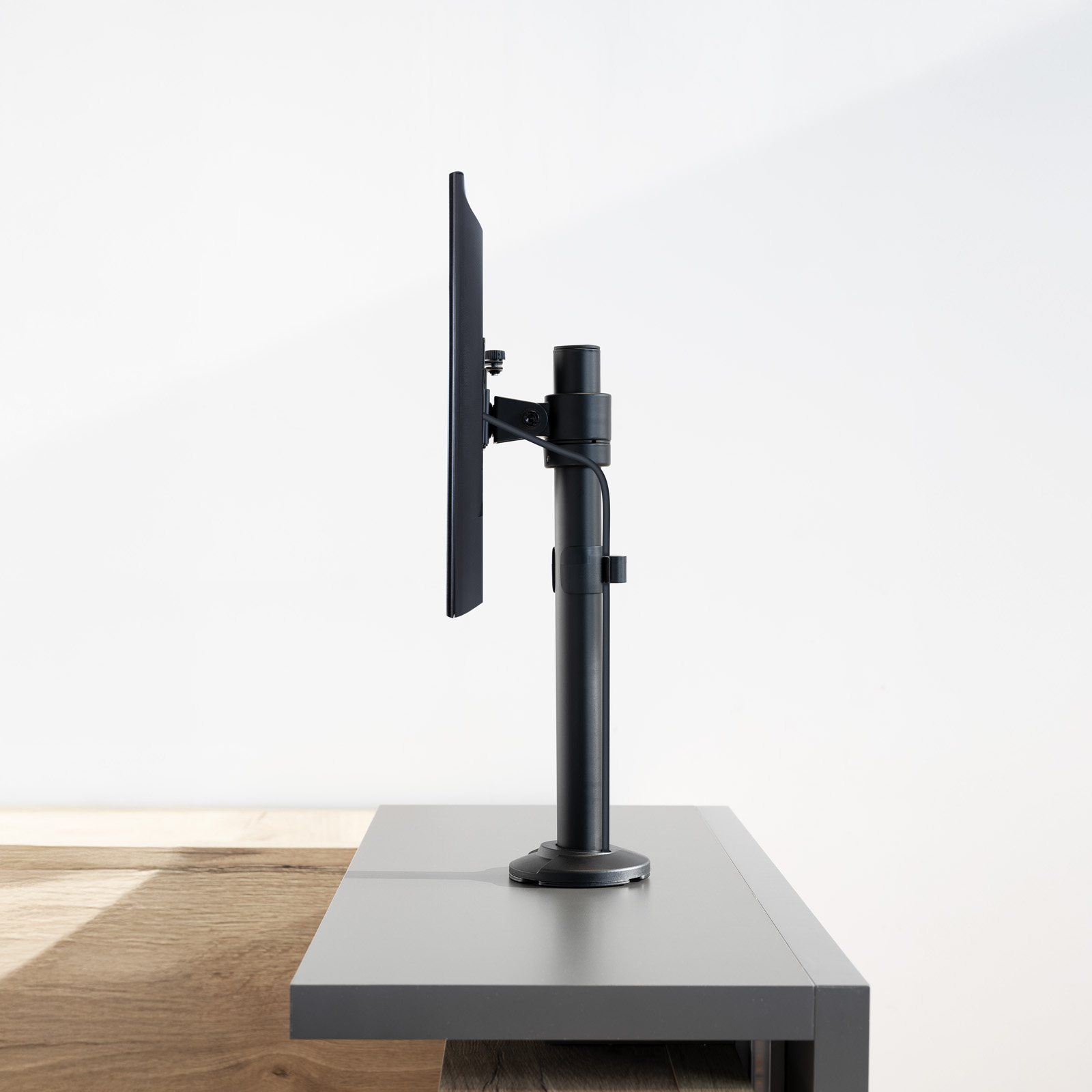 Un monitor montato su un supporto nero. Il supporto è su una scrivania grigia con base in legno. Sfondo bianco.