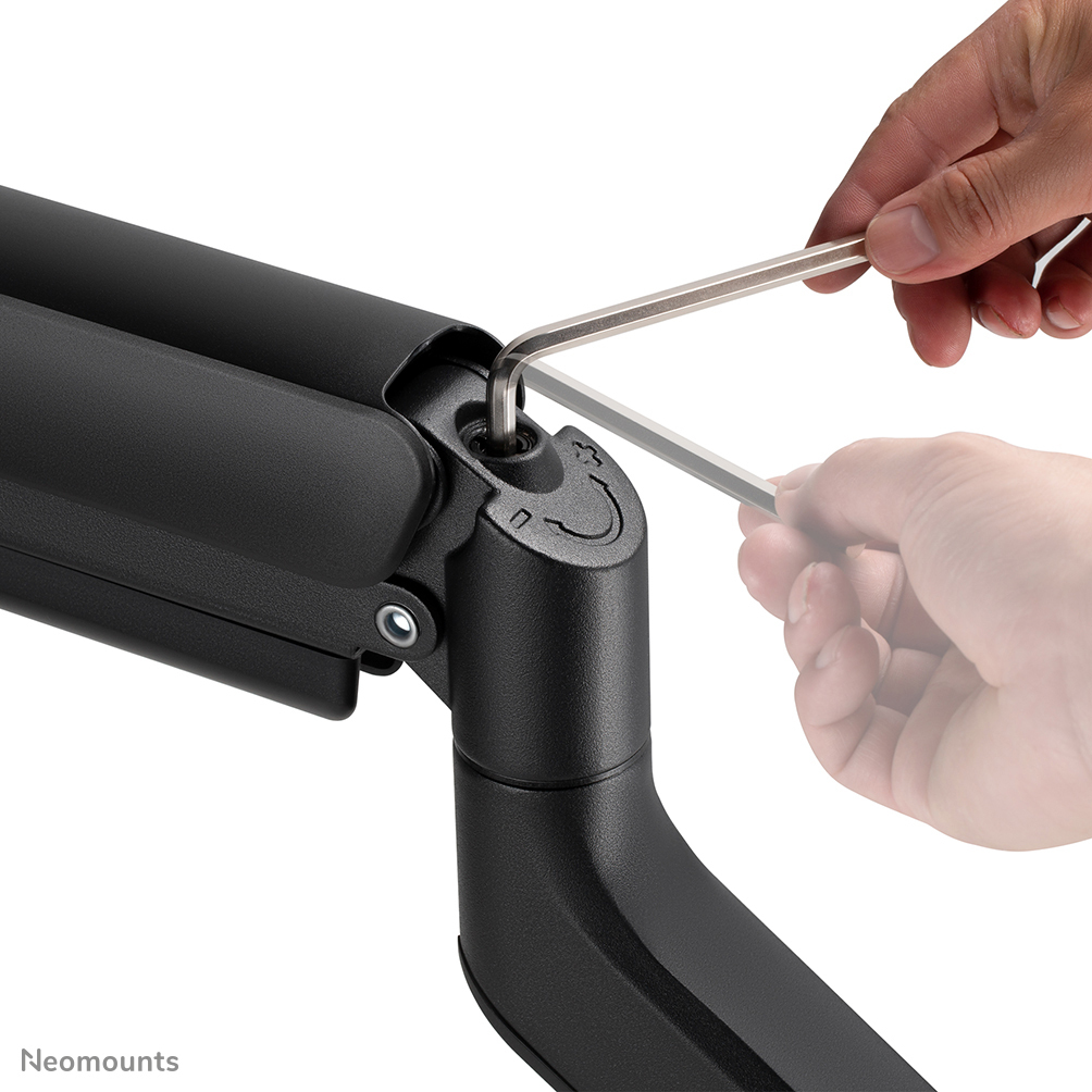 A person uses a hex key to tighten a screw on a black monitor arm. The arm is against a white background.