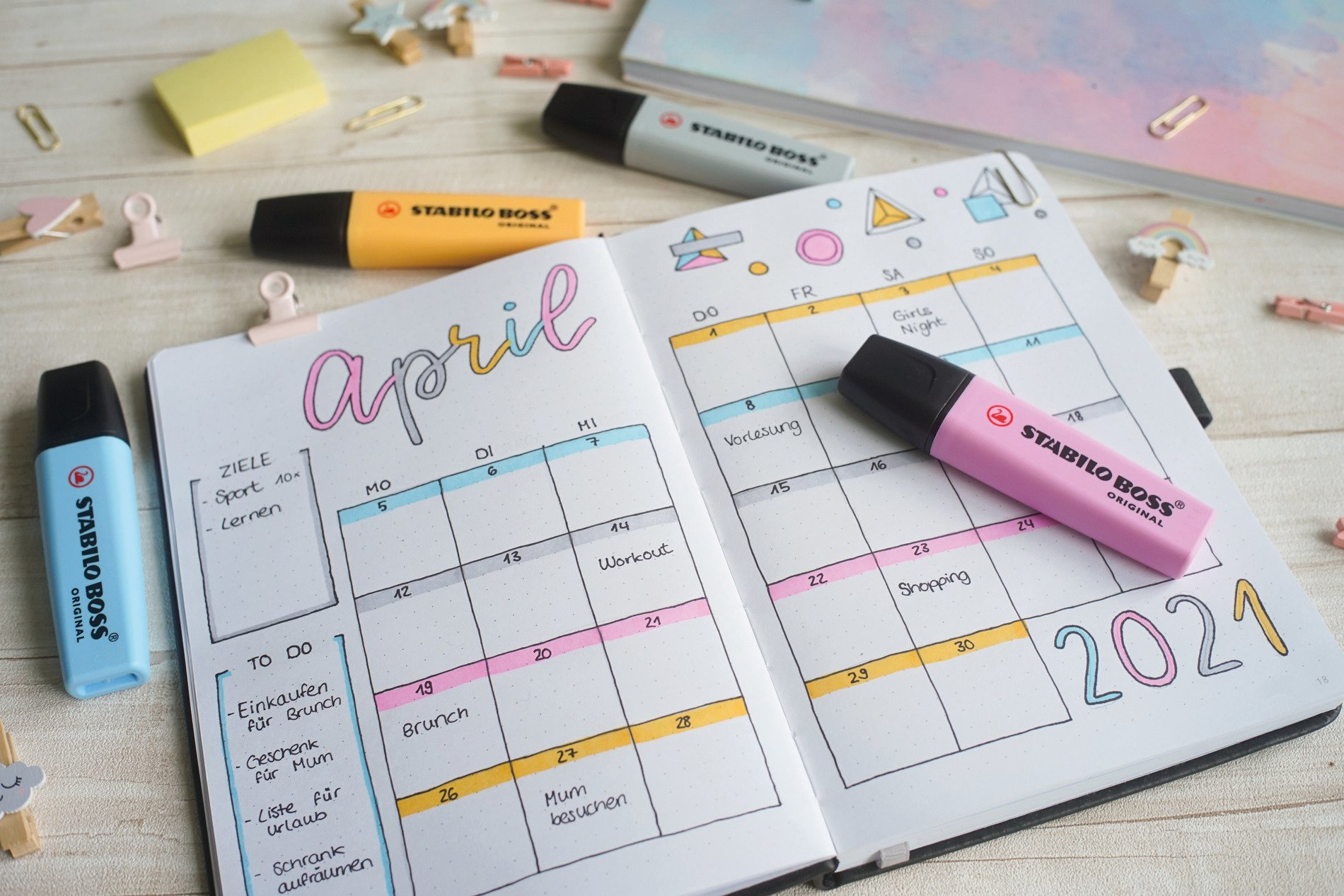 Ein Planer, geöffnet auf April 2021, mit hervorgehobenen Daten, Markern und Bürobedarf auf Holzoberfläche.