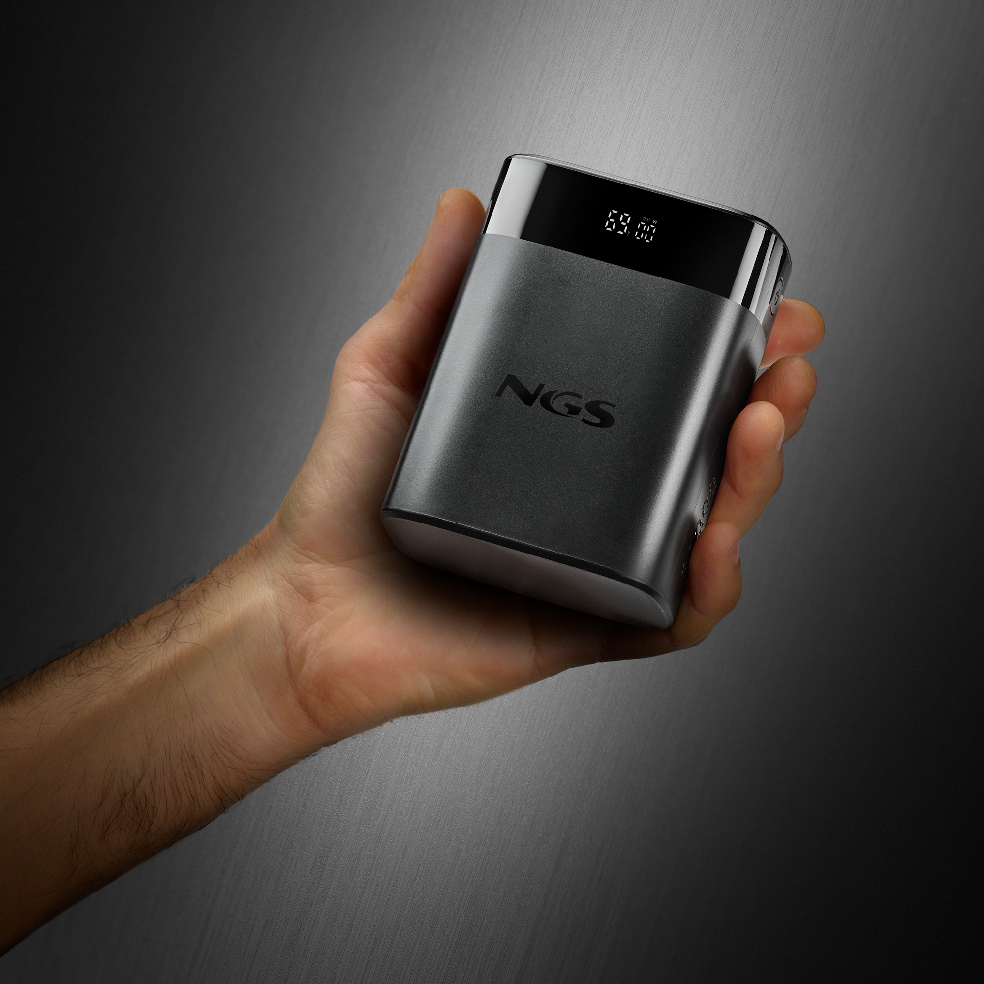 Una mano sostiene un dispositivo rectangular gris oscuro. El dispositivo tiene una parte superior negra con una pantalla digital que muestra '69:00'.