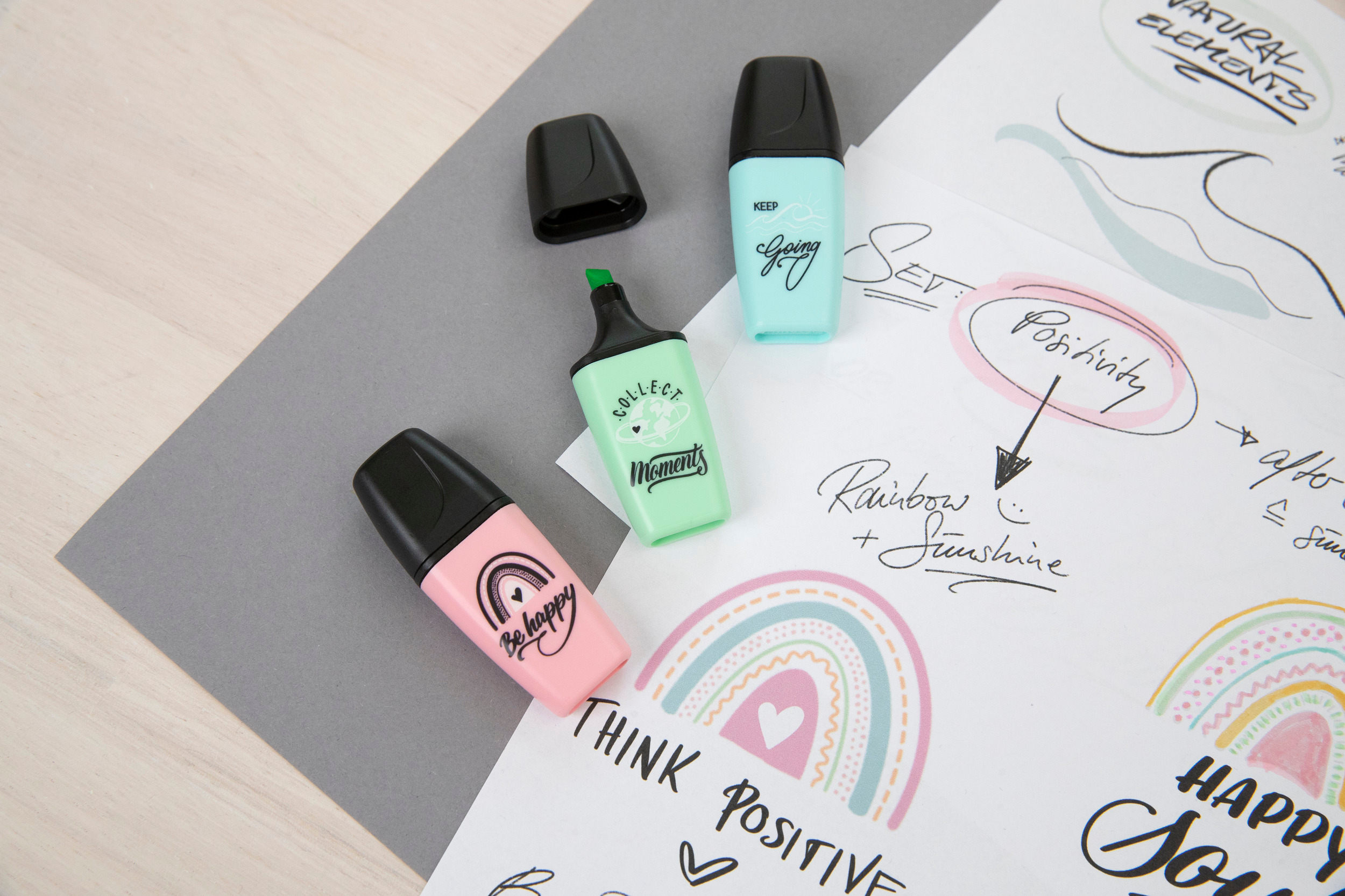 Das Bild zeigt Textmarker, Regenbogenzeichnungen und handschriftlichen Text auf einer grau-weißen Oberfläche.