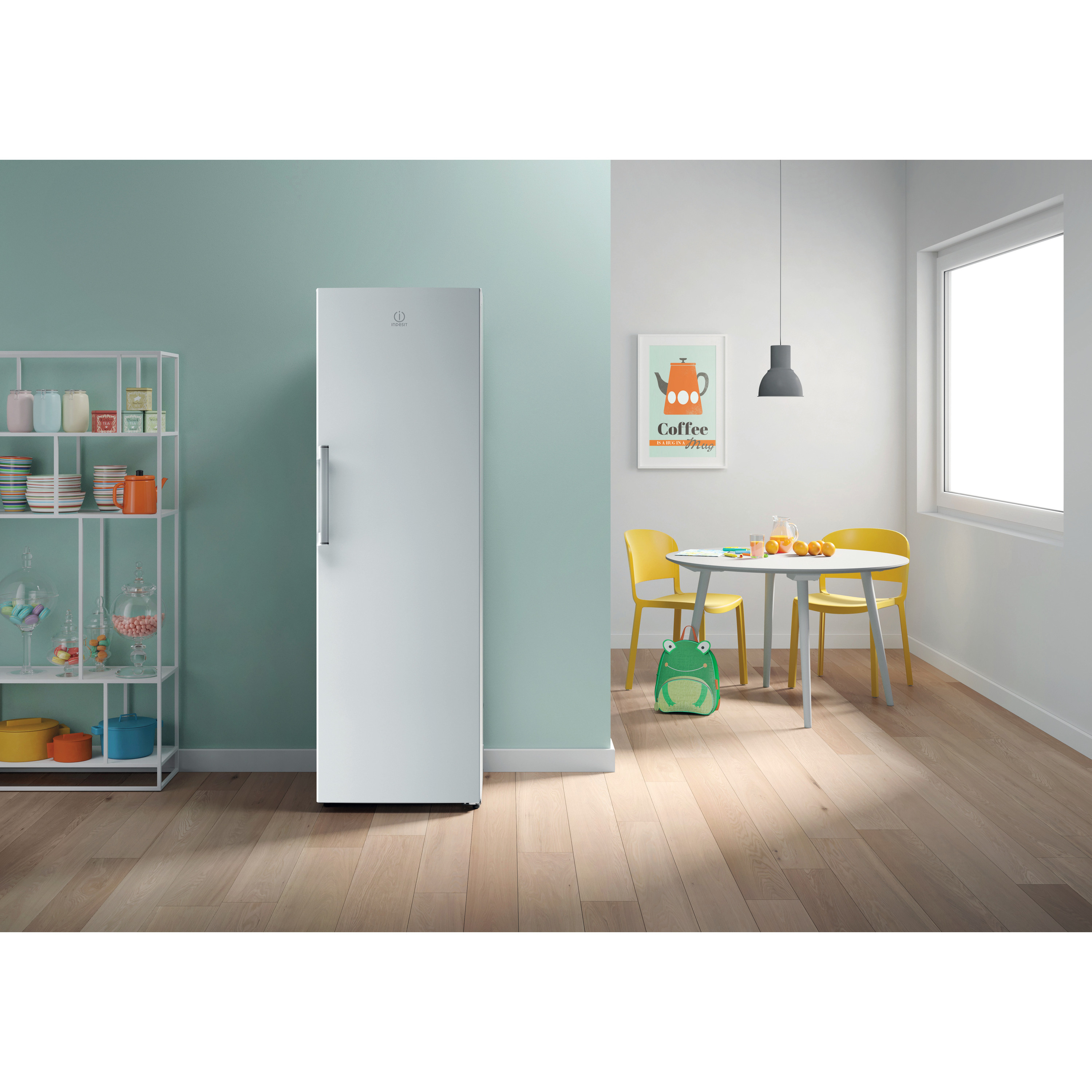 Un refrigerador blanco contra una pared verde azulado. Mesa y sillas a la derecha. Estante con objetos a la izquierda.