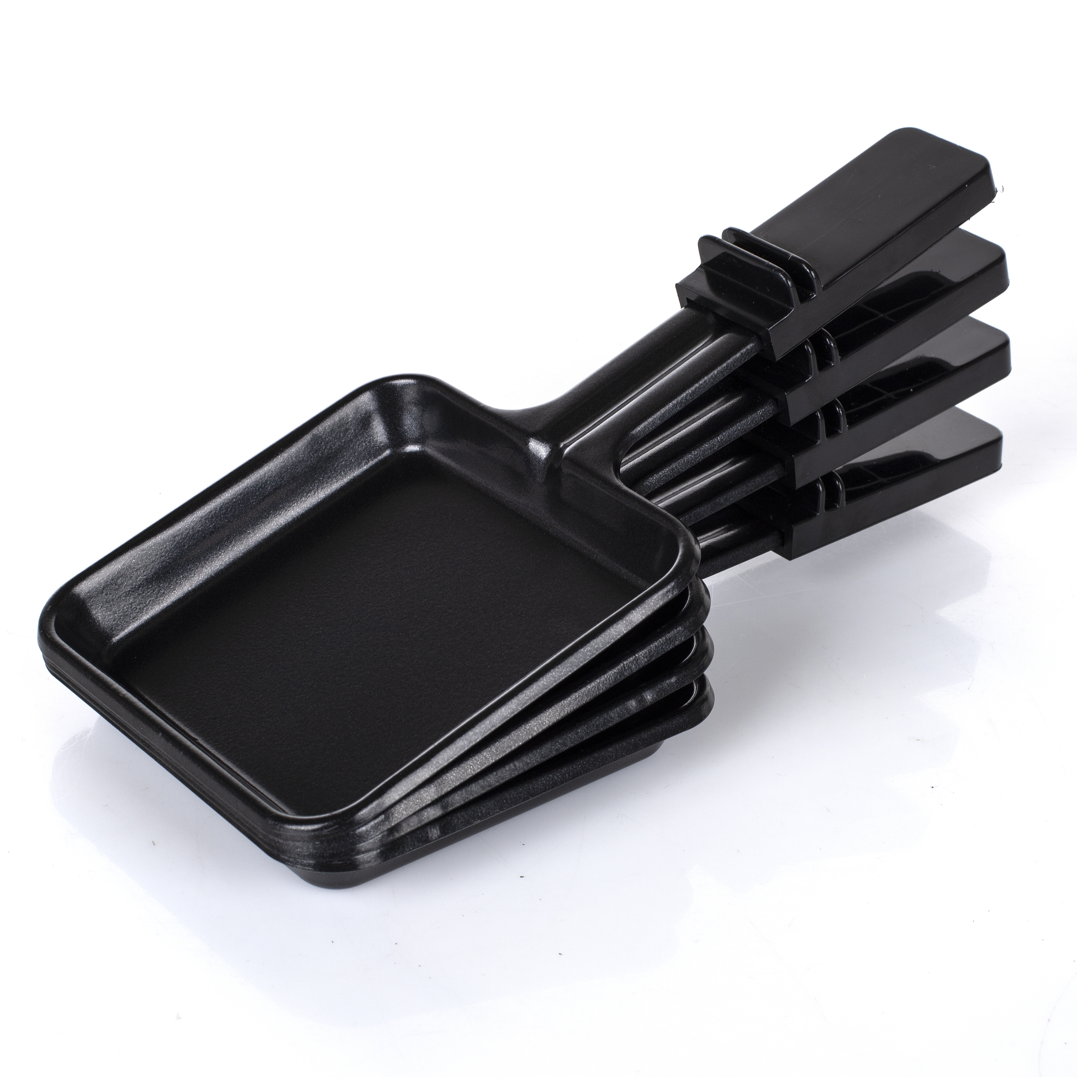 Stos czarnych patelni do raclette. Patelnie są prostokątne z uchwytami. Białe tło.