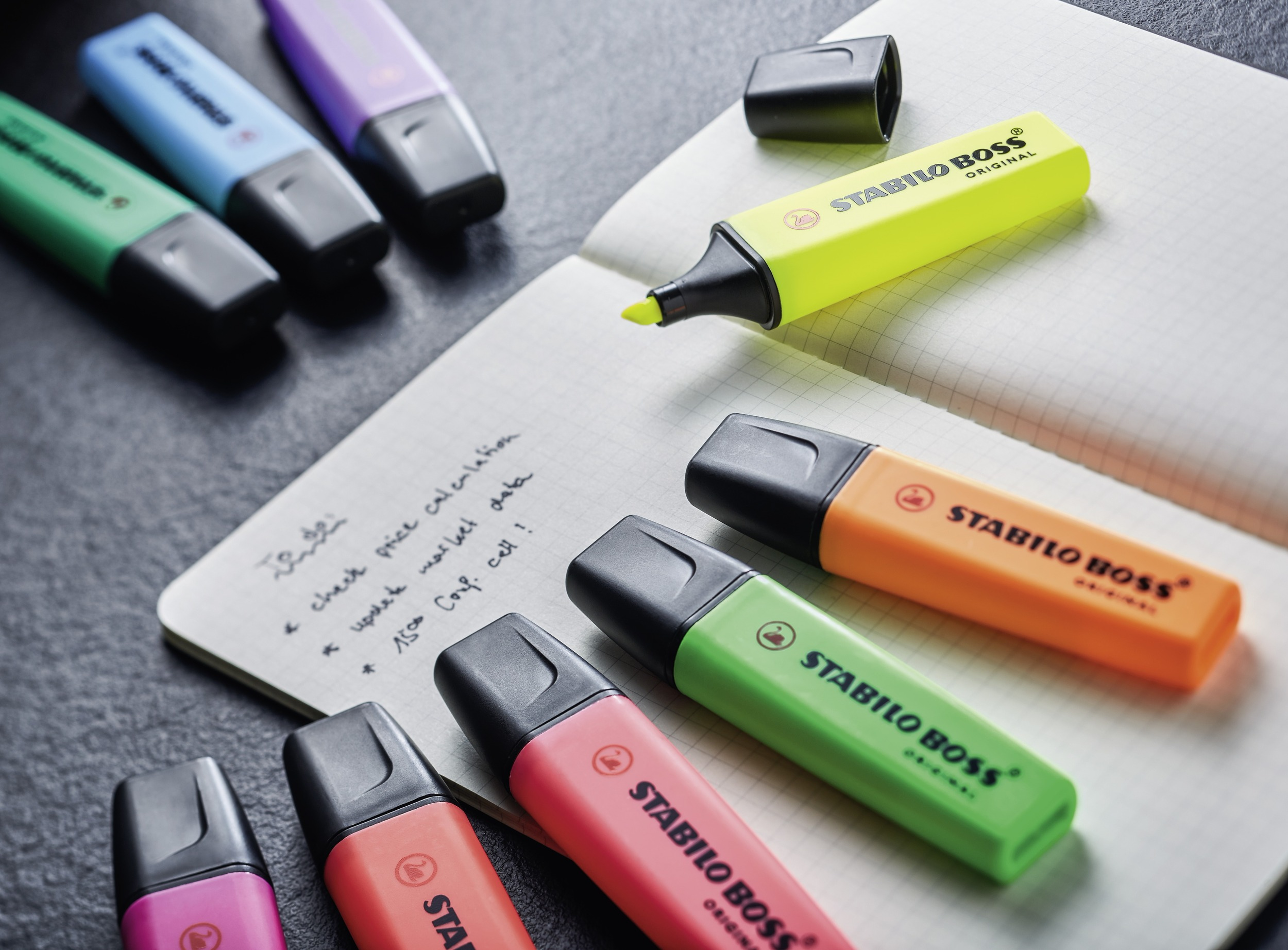 Nahaufnahme von Textmarkern und einem Notizblock. Die Textmarker haben verschiedene Farben, der Notizblock handschriftliche Notizen.