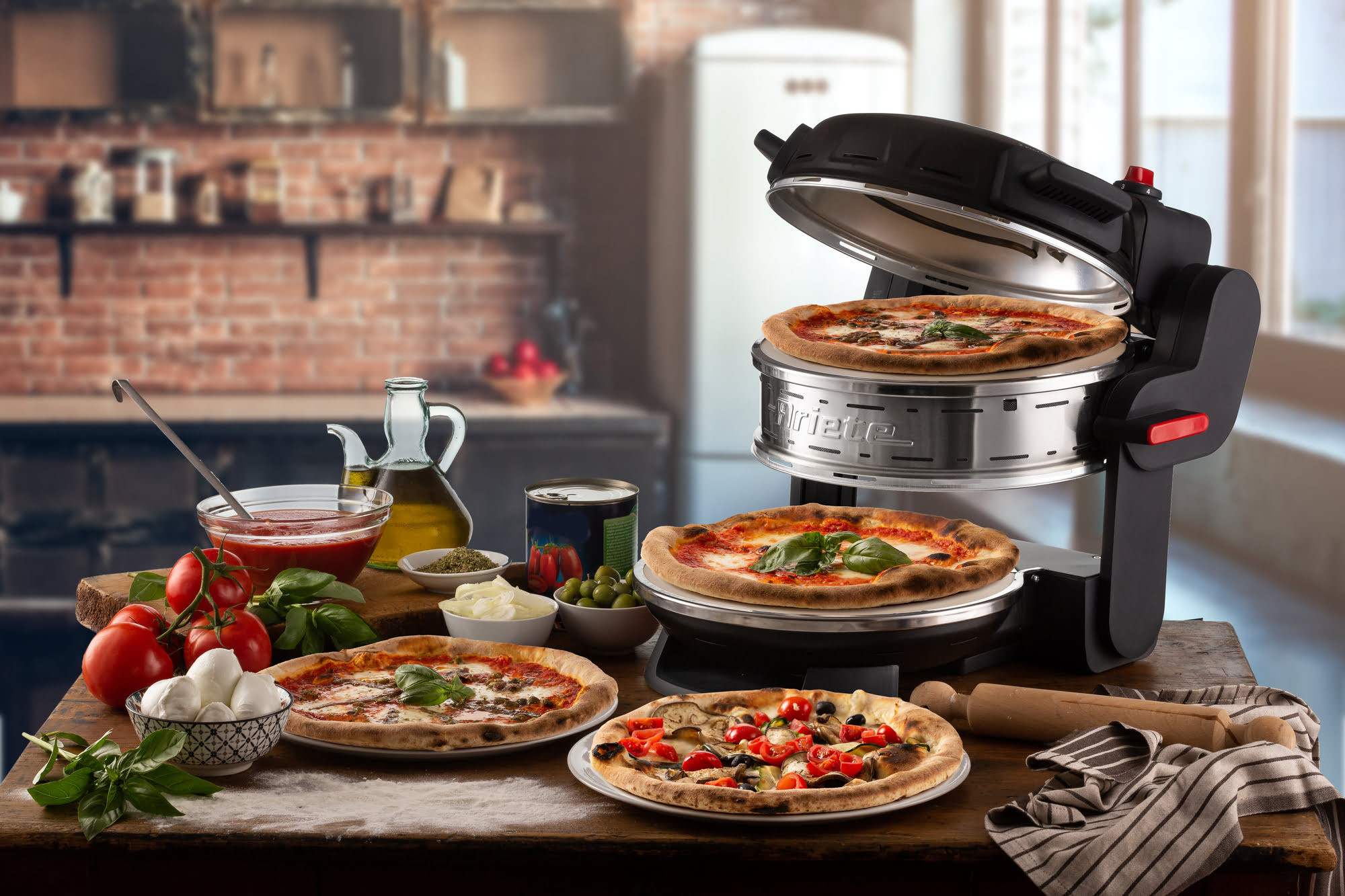 Een tafel met pizza's, ingrediënten en een pizzaoven. Op de achtergrond een keukensetting. De focus ligt op voedselbereiding.