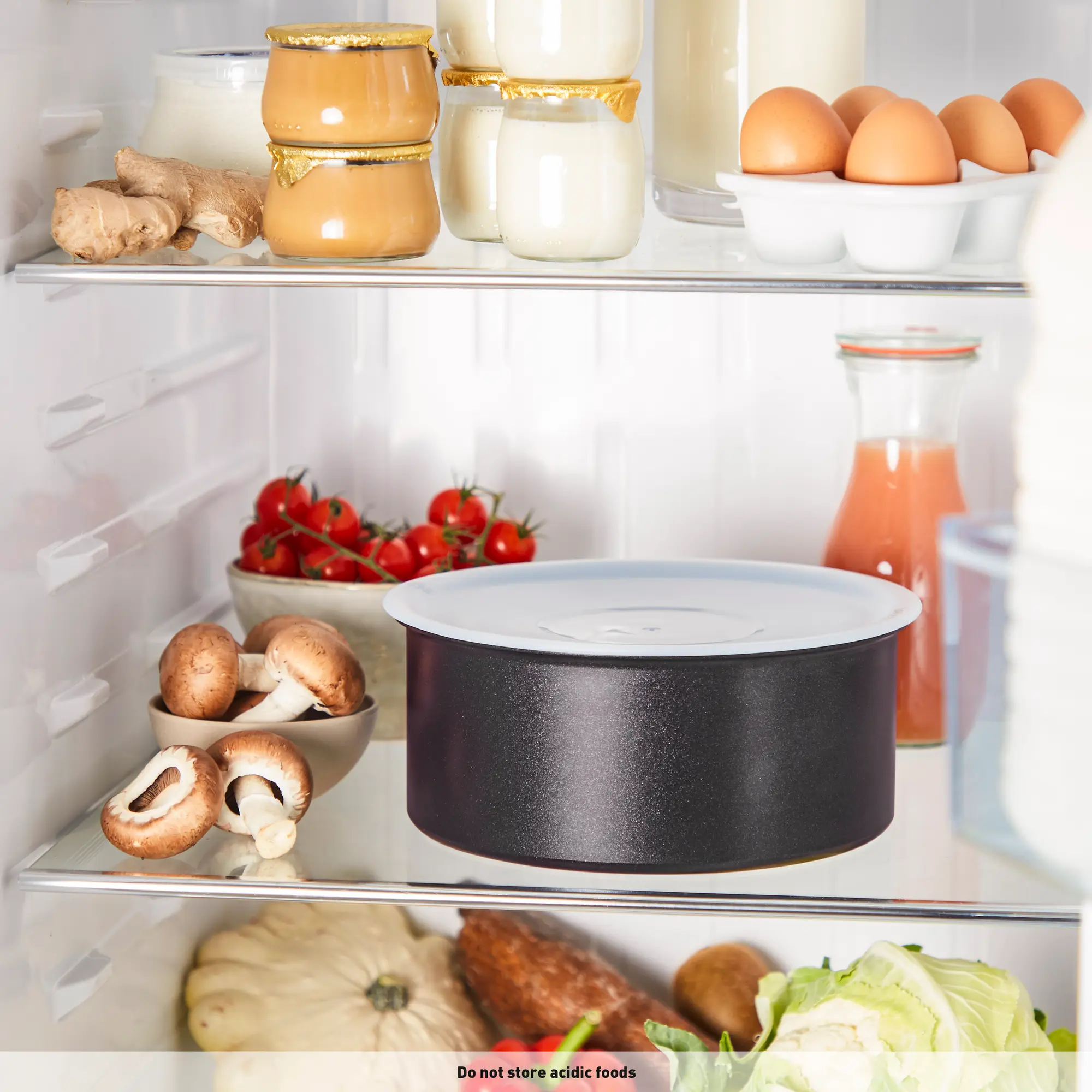 Wnętrze lodówki z jedzeniem: jajka, jogurt, pomidory, grzyby i pojemnik. Warzywa na dole.