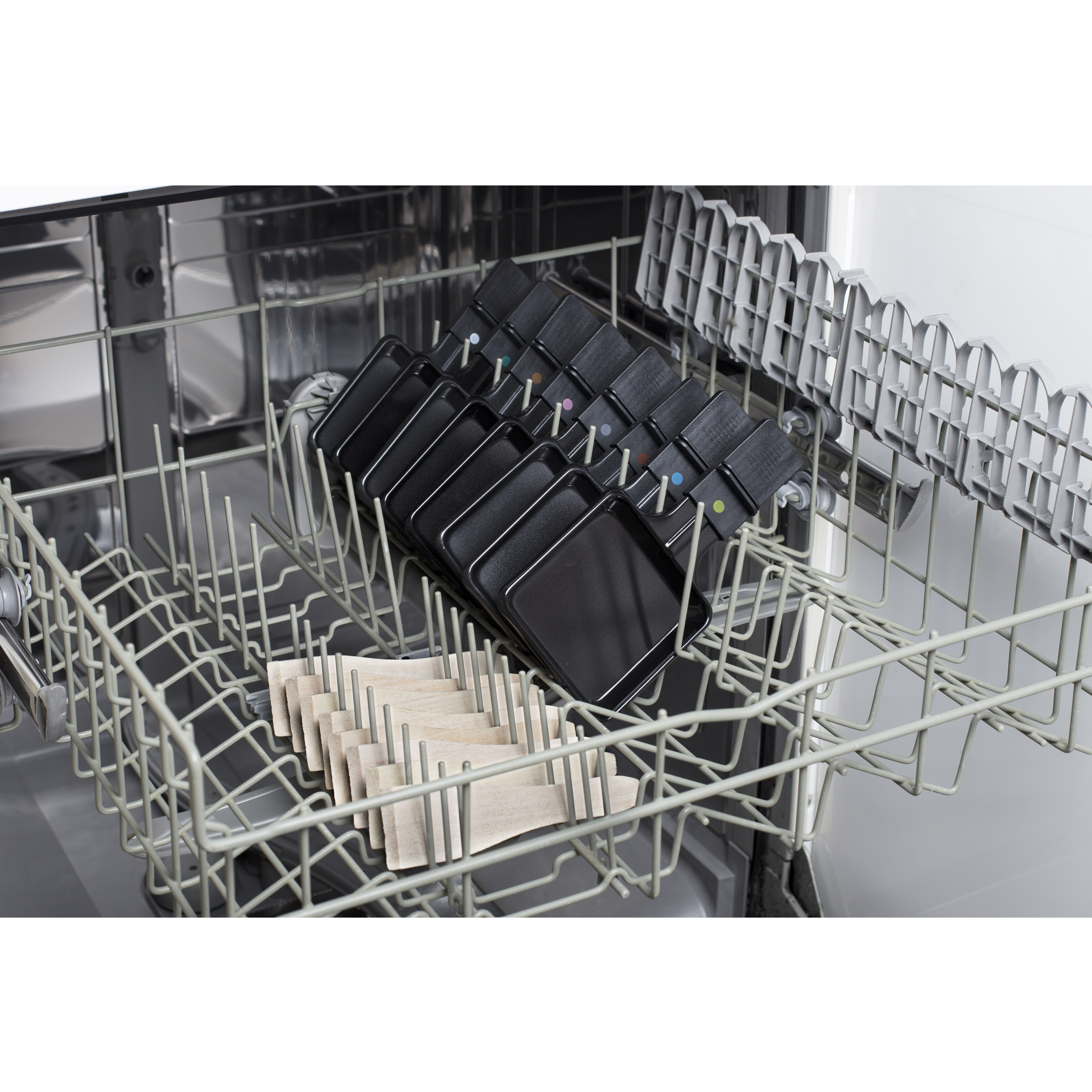 Wnętrze zmywarki z czarnymi patelniami i drewnianymi przedmiotami. Patelnie w górnym koszu, drewno na dole.