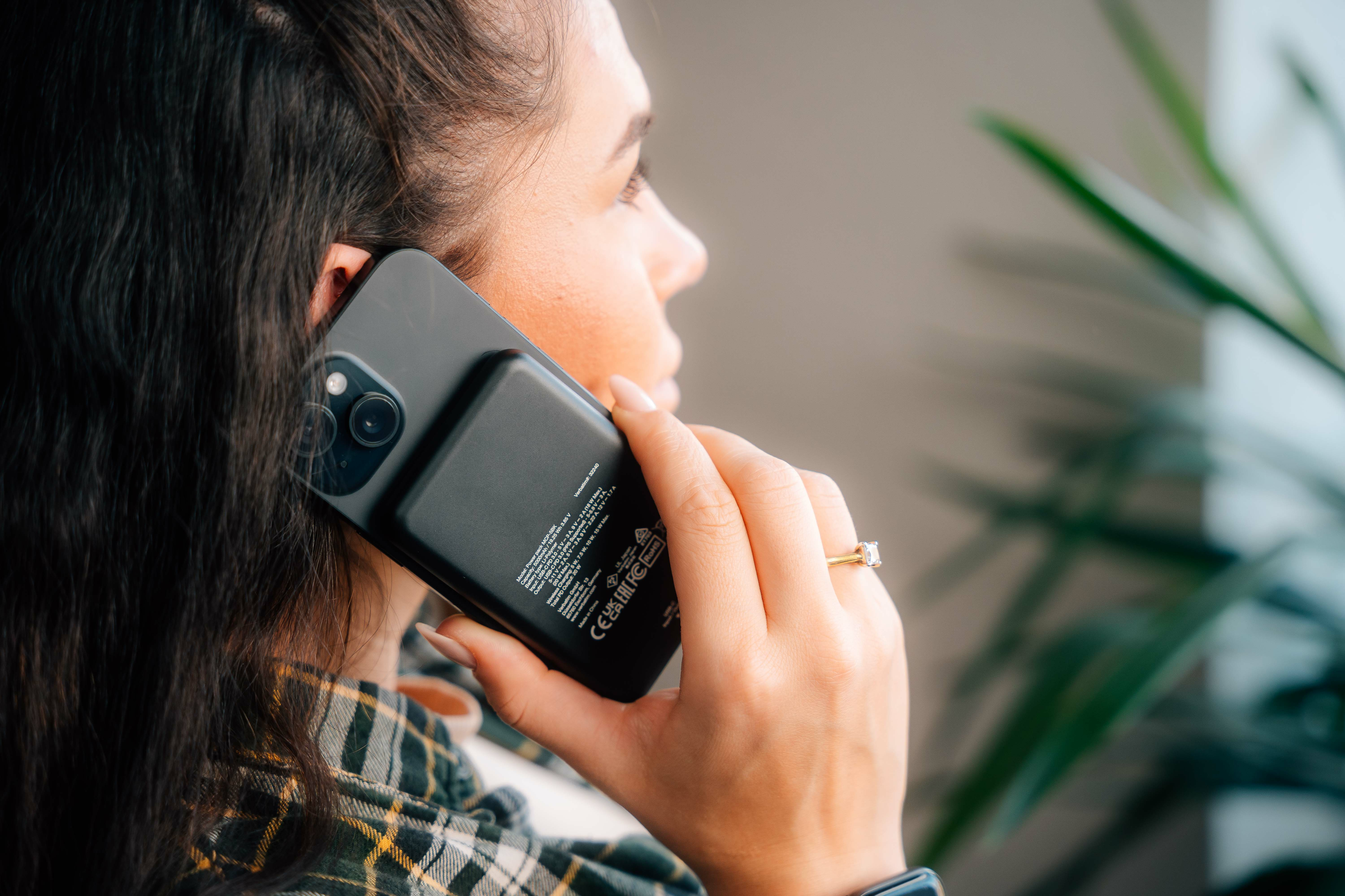 Een vrouw houdt een zwarte telefoon aan haar oor. Ze draagt een geruit overhemd en een ring.