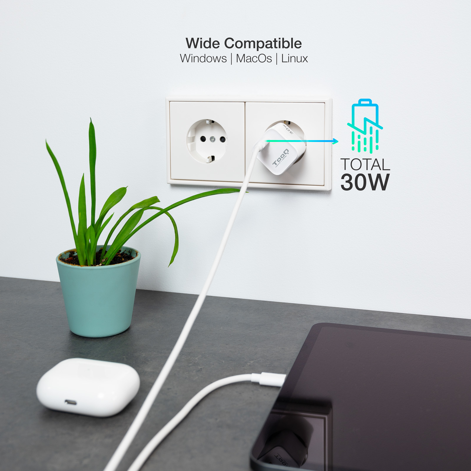 Un cargador blanco está enchufado a una toma de corriente. Una tableta se está cargando. Una pequeña planta está a la izquierda. AirPods están en primer plano.