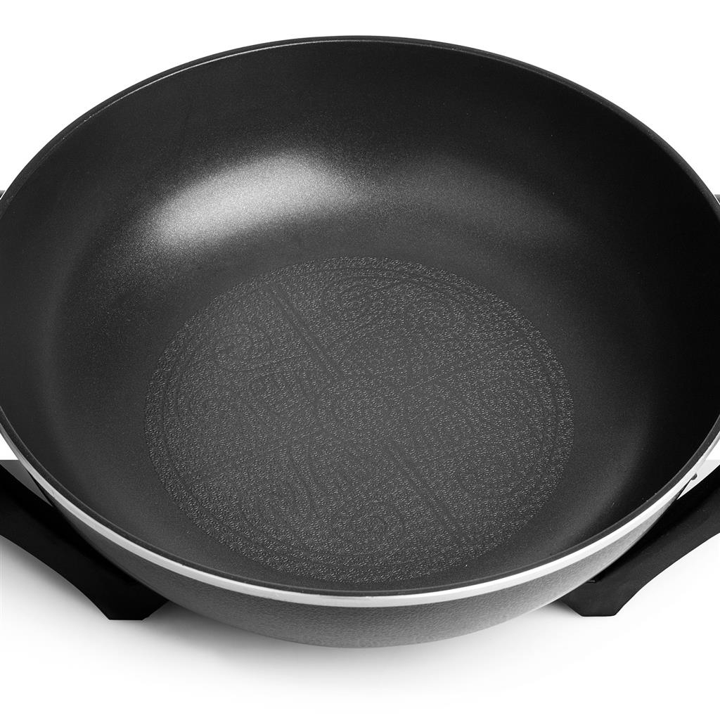 Vista de cerca de un wok negro sobre una superficie blanca. El wok tiene un fondo texturizado y está soportado por un soporte negro.