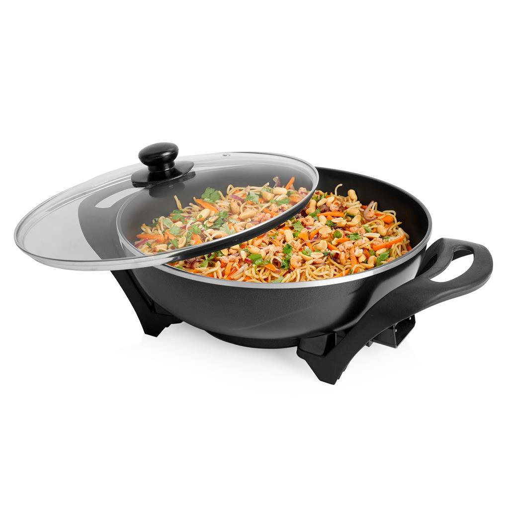 Un wok con fideos, verduras y cacahuetes. Una tapa de cristal está parcialmente abierta. El wok está sobre un soporte negro, fondo blanco.