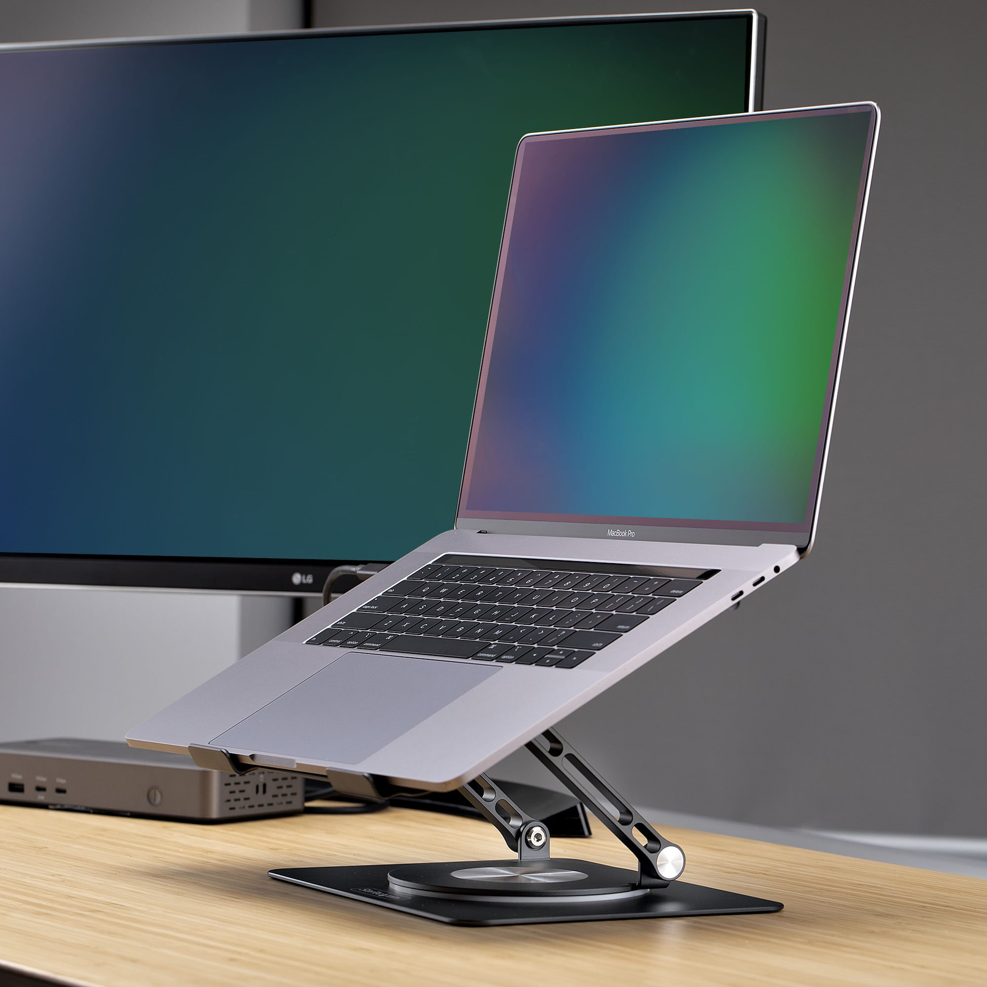 Laptop auf einem Ständer, mit Monitor im Hintergrund. Der Laptop ist geöffnet, Tastatur sichtbar.