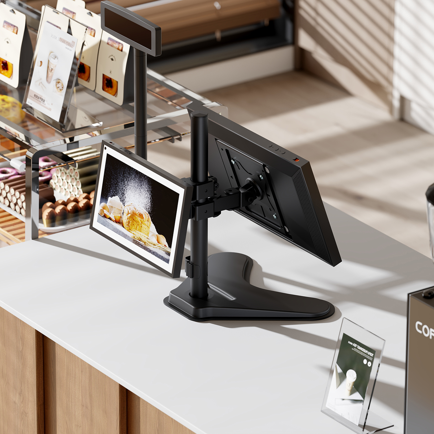 Un bancone di un bar con monitor, pasticcini e segnaletica. Il monitor mostra cibo. È visibile una macchina da caffè.