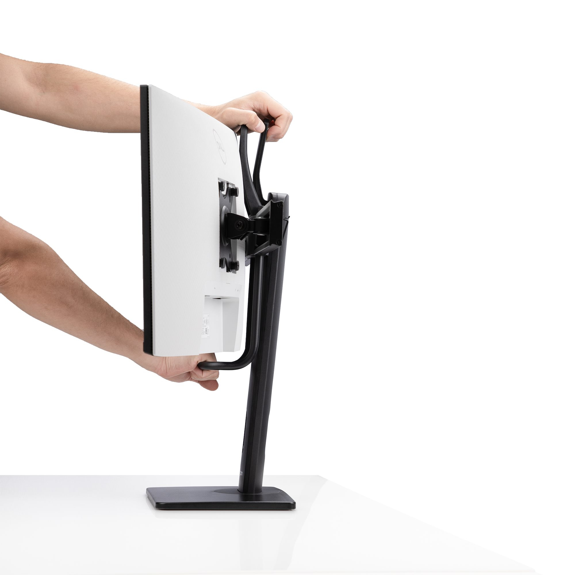 Eine Person hält einen schwarzen Monitorständer mit einem weißen Monitor. Der Ständer steht auf einer weißen Oberfläche.