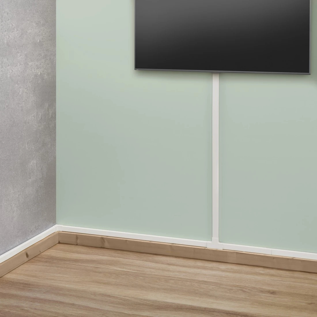 Angolo stanza con parete verde, pavimento in legno e TV nero. Copricavo bianco verticale. Parete grigia a sinistra.
