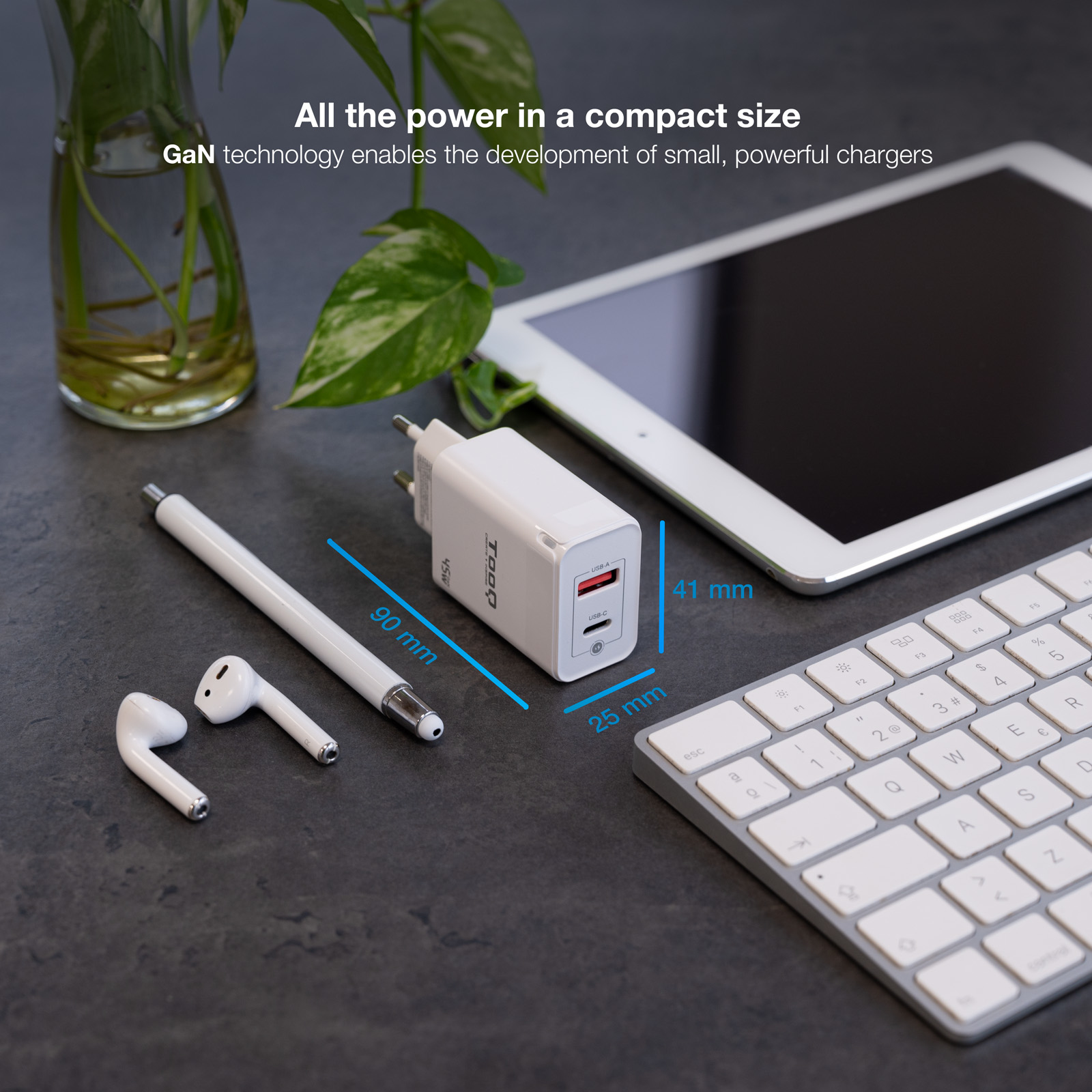 Cargador blanco, auriculares, bolígrafo, tableta y teclado sobre una superficie oscura. Se muestran las dimensiones.