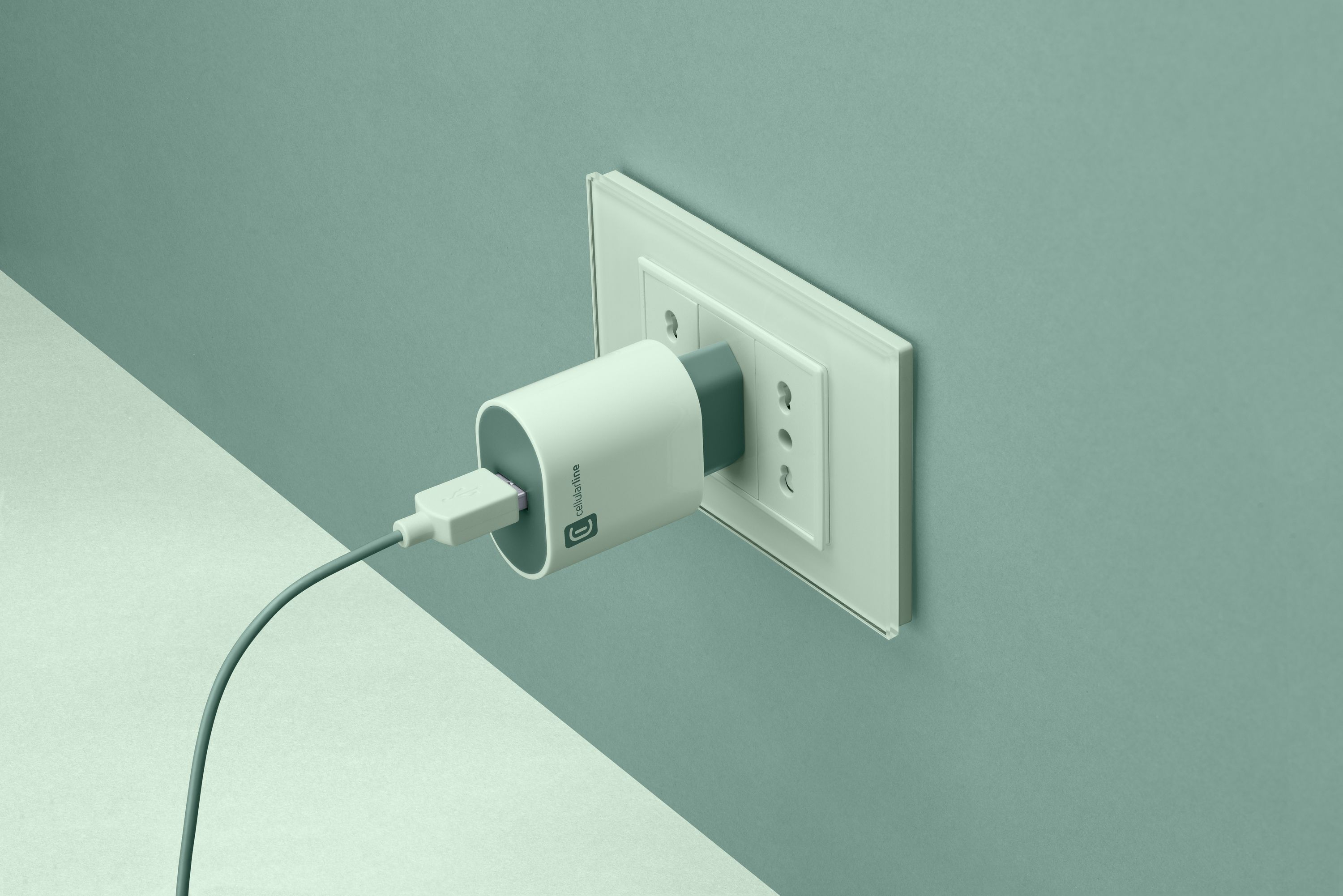 Un cargador blanco está enchufado a un enchufe en una pared verde azulado. Un cable sale del cargador.