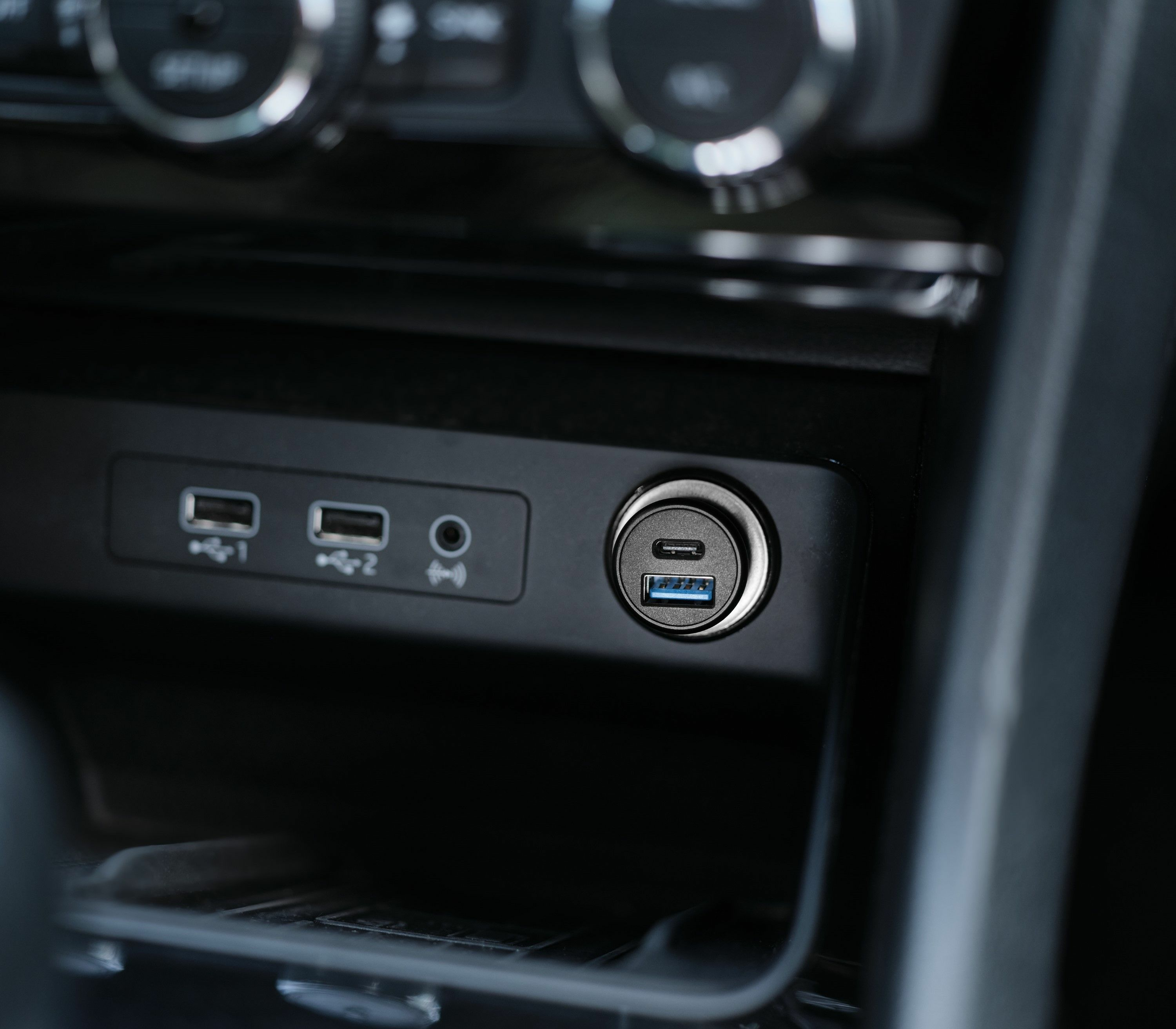 Primer plano del salpicadero de un coche, que muestra puertos USB y un puerto USB-C, todo en plástico negro. Los puertos son azules.