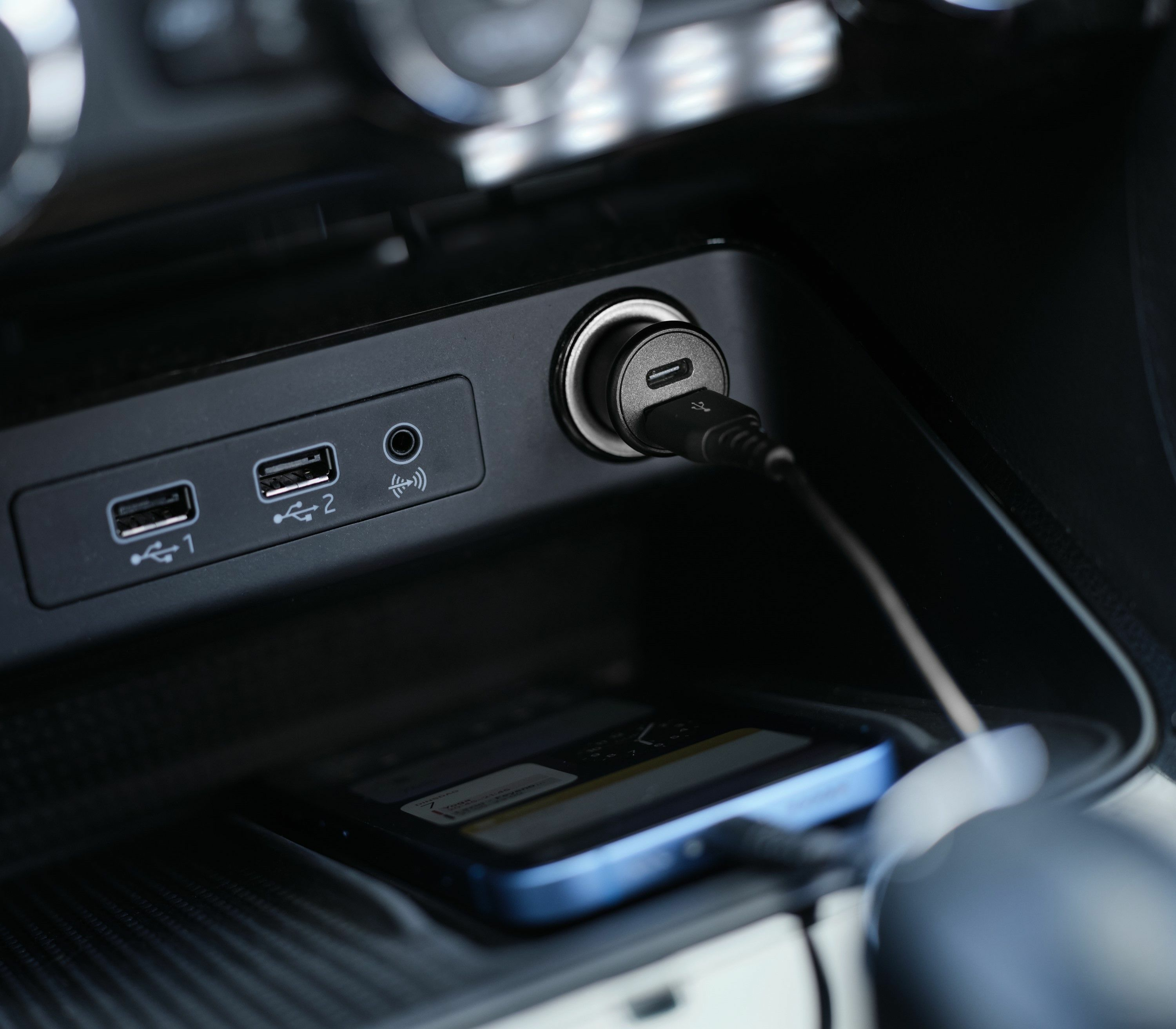 Interior del coche con puertos de carga y un teléfono cargando. Un cable USB-C está enchufado.