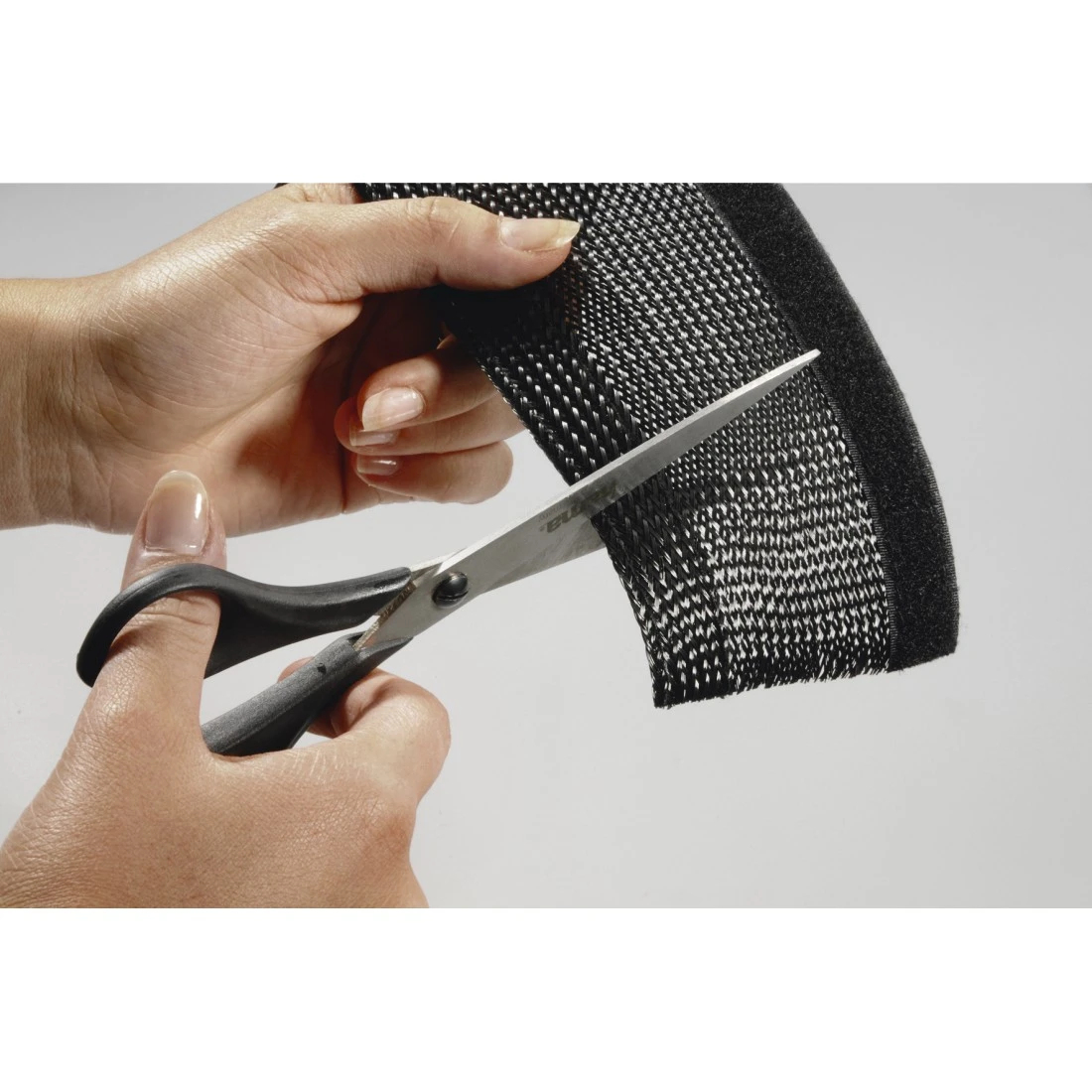 Dłonie tną czarną siatkę nożyczkami. Tkanina ma wzorzystą fakturę. Nożyczki są srebrne i czarne.