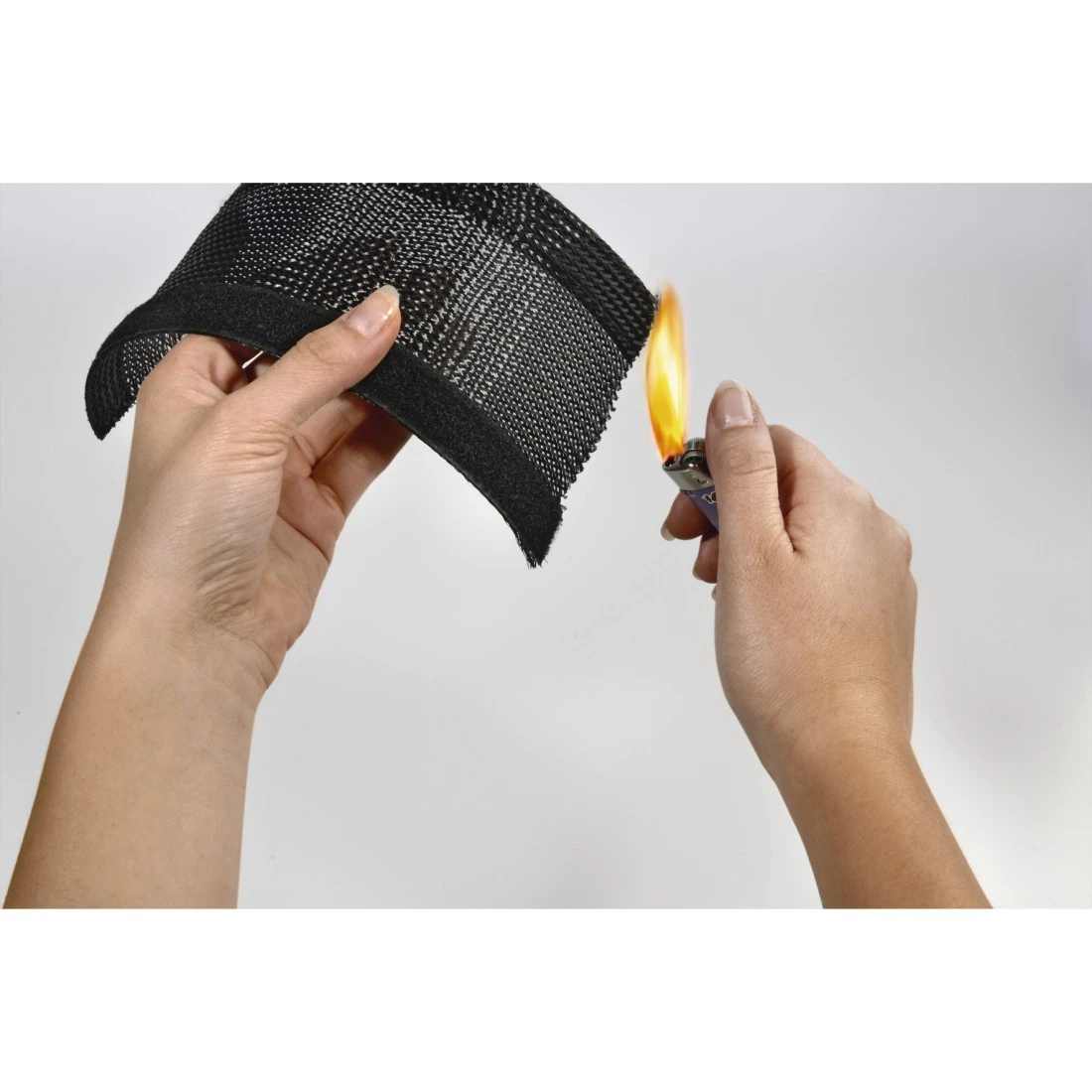Ręce trzymają czarną tkaninę siatkową i zapalniczkę z płomieniem. Tkanina jest testowana ogniem.