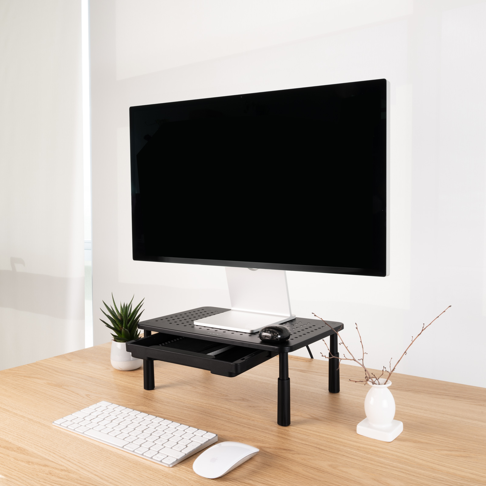 Un'impostazione del computer su una scrivania di legno. Un monitor nero è sopra un supporto nero con un cassetto. Tastiera e mouse sono davanti.